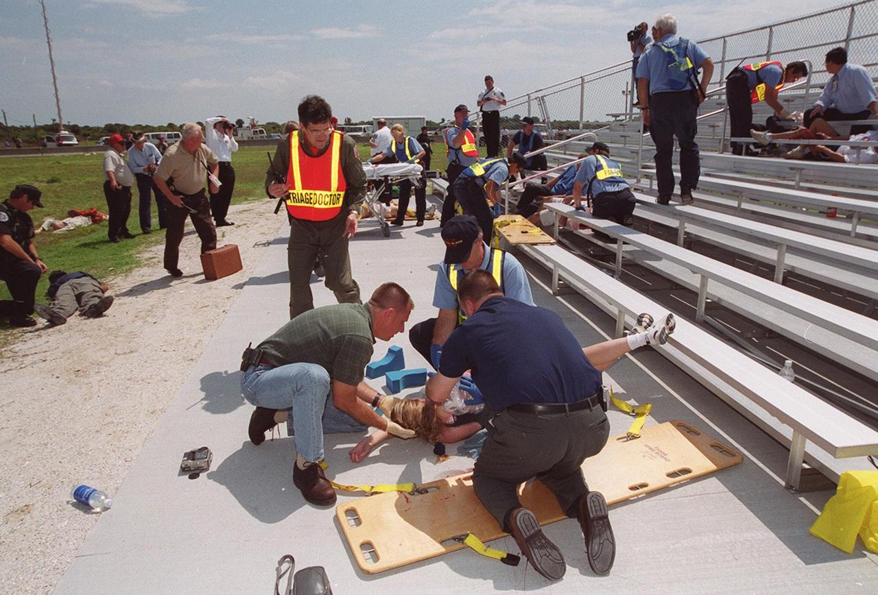 KENNEDY SPACE CENTER, FLA. -- During a staged mass casualty exercise in the Launch Complex 39 area, security and medical personnel take care of a “victim” on the ground by the bleachers. Employees are playing roles in the fictitious sniper attack that is being staged to validate capabilities of KSC’s fire, medical, helicopter transport and security personnel to respond to such an event