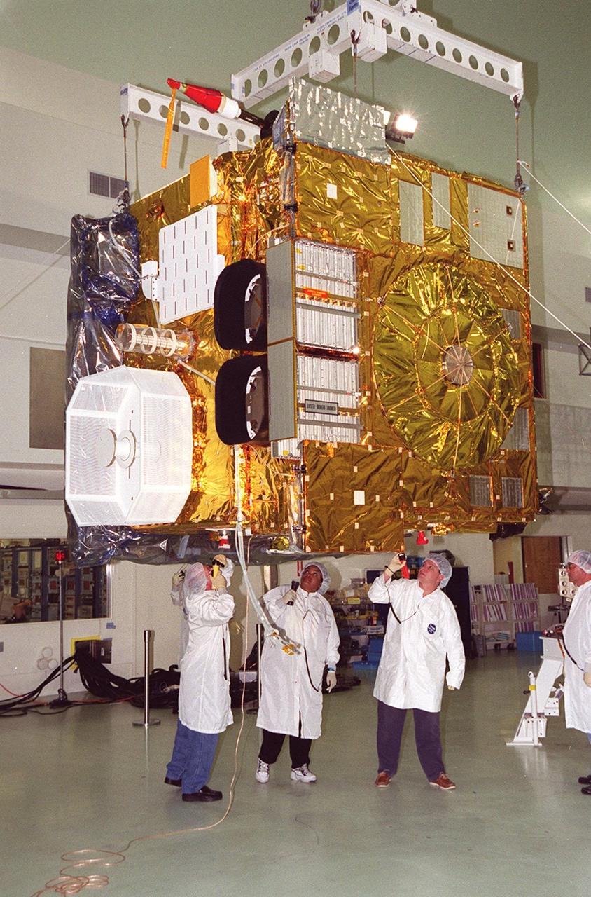 While an overhead crane lifts the GOES-M satellite at Astrotech, Titusville, Fla., workers check the underside. The GOES-M provides weather imagery and quantitative sounding data used to support weather forecasting, severe storm tracking and meteorological research. The satellite is undergoing testing at Astrotech before its scheduled launch July 12 on an Atlas-IIA booster, Centaur upper stage from Cape Canaveral Air Force Station