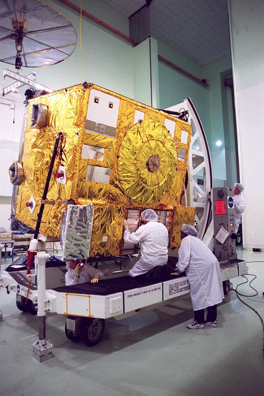 With the GOES-M satellite tilted on a workstand at Astrotech, Titusville, Fla, workers check out a part of the underside. The GOES-M provides weather imagery and quantitative sounding data used to support weather forecasting, severe storm tracking and meteorological research. The satellite is undergoing testing at Astrotech before its scheduled launch July 12 on an Atlas-IIA booster, Centaur upper stage from Cape Canaveral Air Force Station