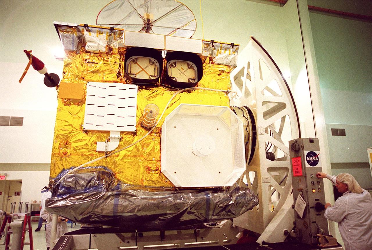 At Astrotech, Titusville, Fla., a worker (right) turns the GOES-M satellite, bringing its side into view. The GOES-M provides weather imagery and quantitative sounding data used to support weather forecasting, severe storm tracking and meteorological research. The satellite is undergoing testing at Astrotech before its scheduled launch July 12 on an Atlas-IIA booster, Centaur upper stage from Cape Canaveral Air Force Station