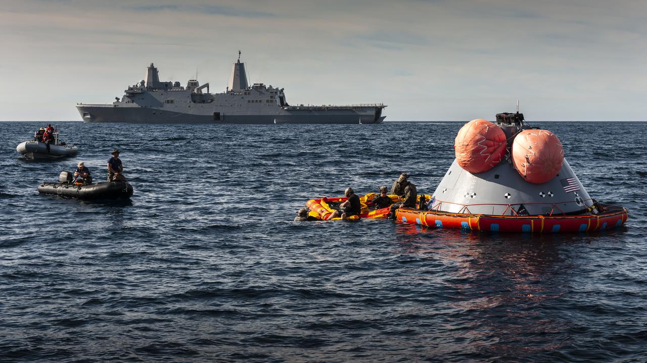 U.S. Navy divers prepare to attach the "front porch" to a test version of the Orion capsule on Nov. 1, 2018, as part of Underway Recovery Test-7 (URT-7) in the open water of the Pacific Ocean. Nearby is the USS John P. Murtha. Orion will be towed into the ship's well deck. There are two large, orange mockup uprighting bags in this view, but when Orion actually splashes down there will be five. URT-7 is one in a series of tests that the Exploration Ground Systems Recovery Team, along with the U.S. Navy, are conducting to verify and validate procedures and hardware that will be used to recover the Orion spacecraft after it splashes down in the Pacific Ocean following deep space exploration missions. Orion will have emergency abort capability, sustain the crew during space travel and provide safe re-entry from deep space return velocities.