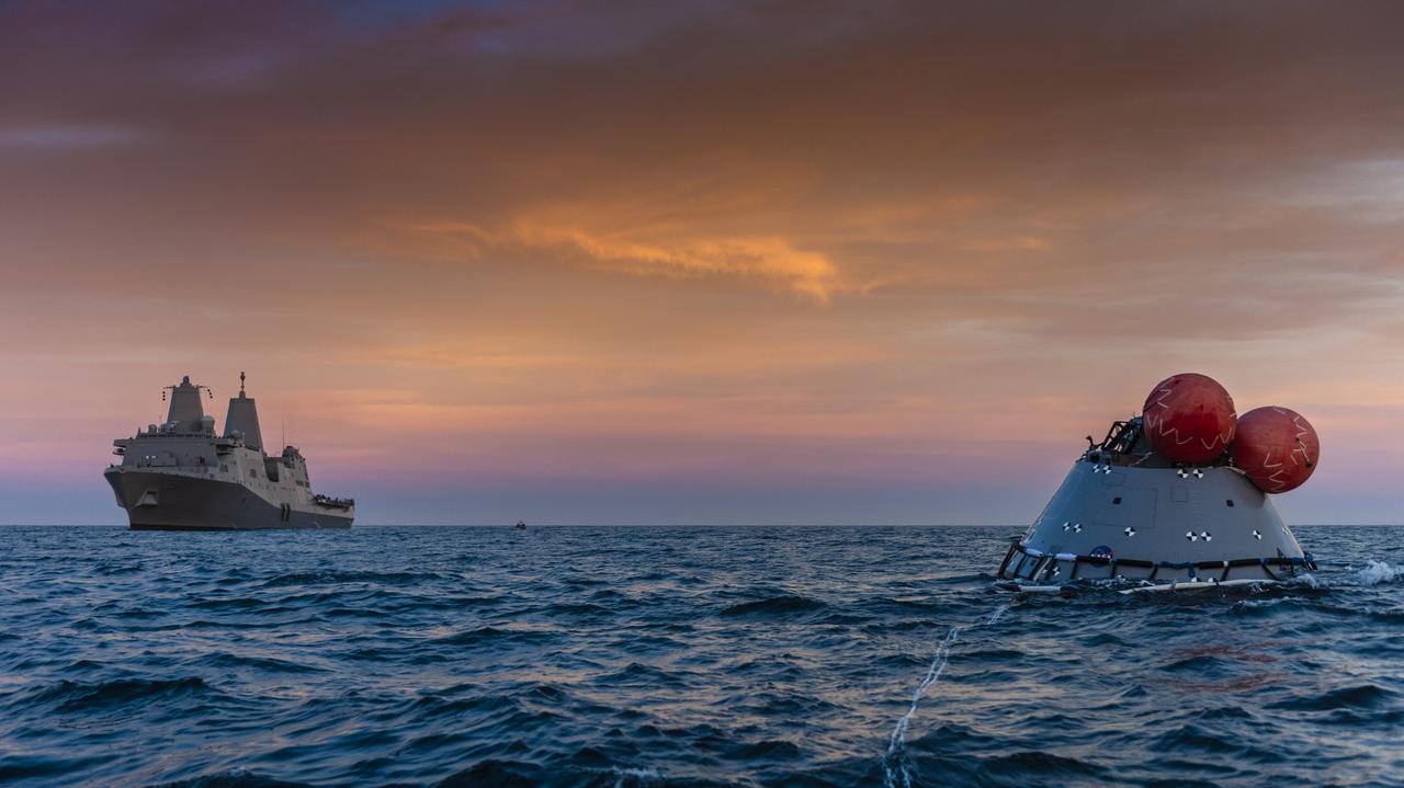 At sunset, a test version of the Orion capsule floats in the Pacific Ocean on Nov. 1, 2018, during Underway Recovery Test-7 (URT-7). Nearby is the USS John P. Murtha. Orion will be towed into the ship's well deck. URT-7 is one in a series of tests that the Exploration Ground Systems Recovery Team, along with the U.S. Navy, are conducting to verify and validate procedures and hardware that will be used to recover the Orion spacecraft after it splashes down in the Pacific Ocean following deep space exploration missions. Orion will have emergency abort capability, sustain the crew during space travel and provide safe re-entry from deep space return velocities.