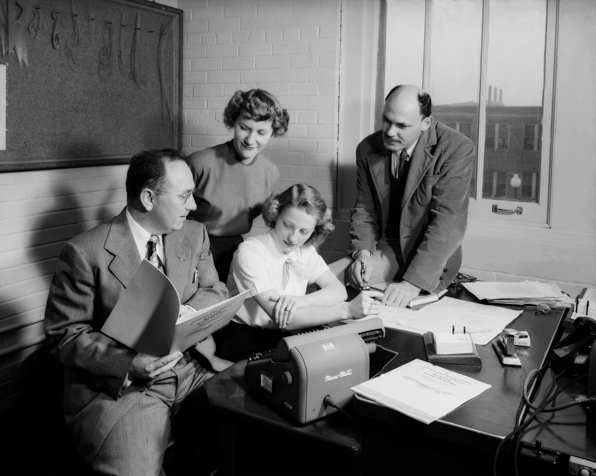 Two men and two women gather around a machine on a desk.