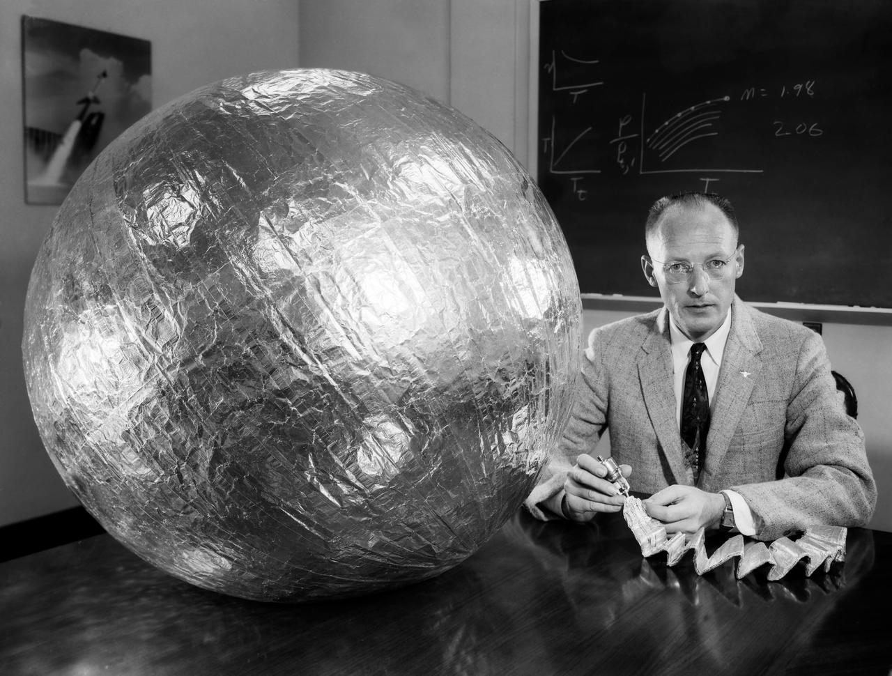  Engineer W.J. O Sullivan, Jr., seated beside 30 inch subsatellite. He holds inflation bottle and folded duplicate copy, July 1957. 