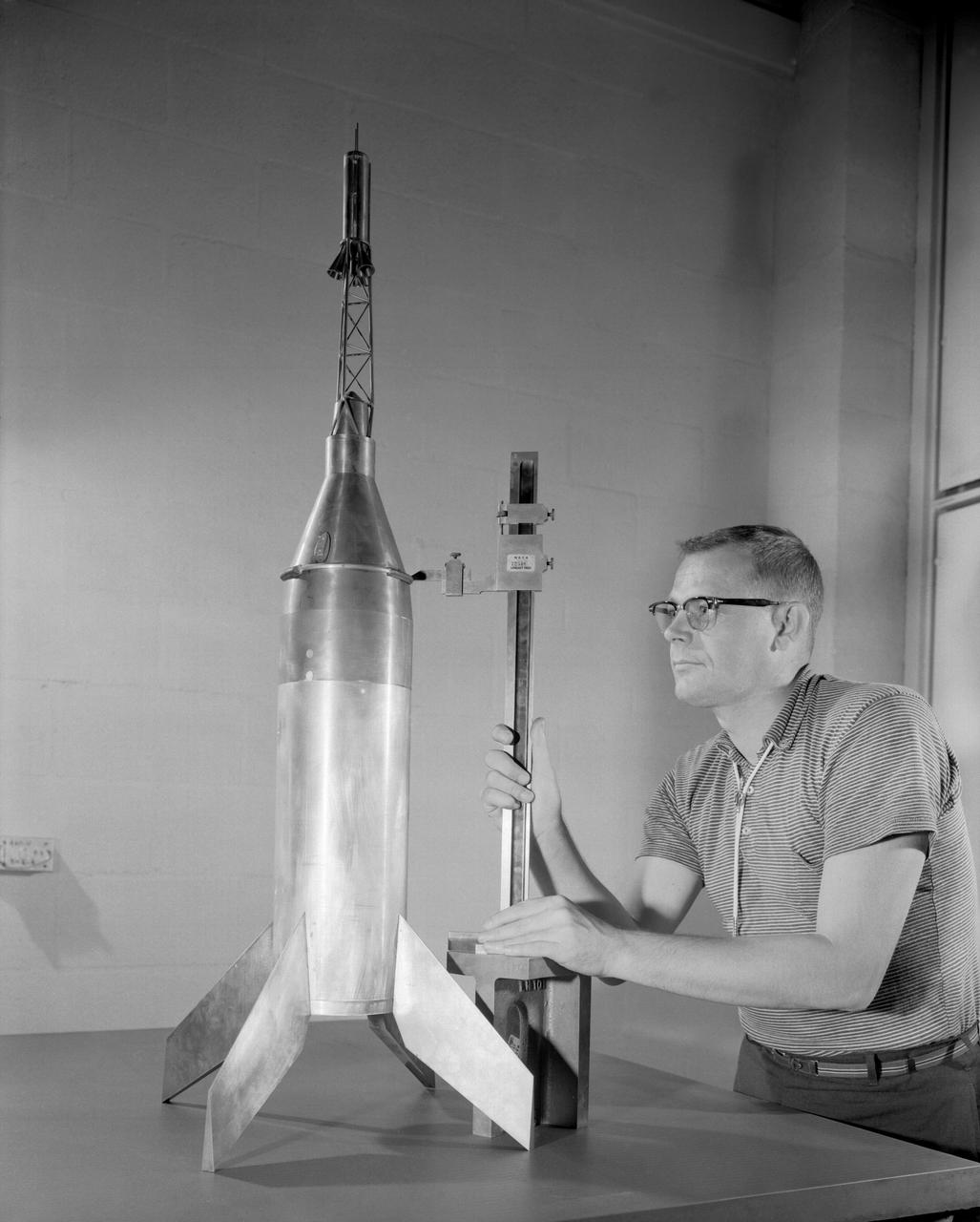 Publicity photograph of a technician measuring a wind tunnel model of the Little Joe test vehicle. Joseph Shortal noted that (vol. 3, p. 29):  The largest project at Wallops in support of Mercury was the Little Joe project, designed to qualify the abort-escape system under flight conditions.  James Hansen (p. 47) writes:  STG engineers Max Faget and Paul Purser, then of Langley's PARD, had conceived Little Joe as a space capsule test vehicle even before the establishment of NASA and the formation of the STG. Girlruth understood the importance of the Little Joe tests:  We had to be sure there were no serious performance and operational problems that we had simply not thought of in such a new and radical type of flight vehicle.  -- Published in James R. Hansen, Spaceflight Revolution: NASA Langley Research Center From Sputnik to Apollo, (Washington: NASA, 1995), p. 47  Joseph A. Shortal, History of Wallops Station: Origins and Activities Through 1949, (Wallops Island, VA: National Aeronautics and Space Administration, Wallops Station, nd), Comment Edition.