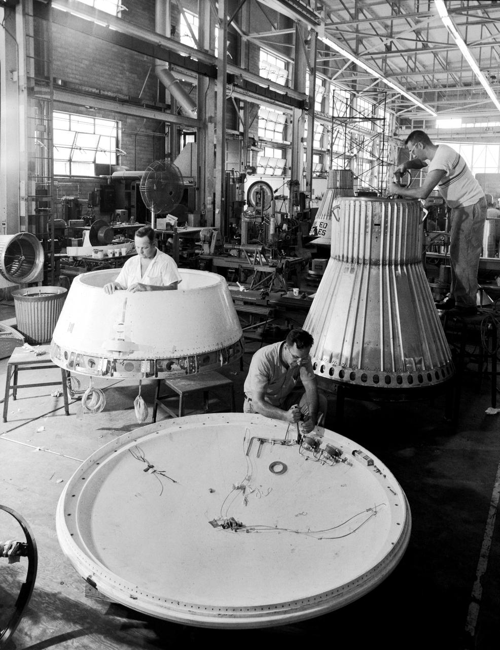 Assembling the Little Joe capsules.  The capsules were manufactured  in-house  by Langley technicians. Three capsules are shown here in various stages of assembly. The escape tower and rocket motors shown on the completed capsule would be removed before shipping and finally assembly for launching at Wallops Island. Joseph Shortal wrote (vol. 3, p. 32):  Design of the Little Joe capsules began at Langley before McDonnell started on the design of the Mercury capsule and was, therefore, a separate design. Although it was not designed to carry a man, it did have to carry a monkey. It had to meet the weight and center of gravity requirements of Mercury and withstand the same aerodynamic loads during the exit trajectory.   Although in comparison with the overall Mercury Project, Little Joe was a simple undertaking, the fact that an attempt was made to condense a normal two-year project into a 6-month one with in house labor turned it into a major undertaking for Langley.  Project Mercury: Little Joe: Boilerplate Mercury spacecraft undergo fabrication at the shops of the Langley Research Center. They will launched atop Little Joe rockets to test the spacecraft recovery systems. -- Published in Joseph A. Shortal, History of Wallops Station: Origins and Activities Through 1949, (Wallops Island, VA: National Aeronautics and Space Administration, Wallops Station, nd), Comment Edition. L59-4947 Technicians prepare a Little Joe launch vehicle prototype for the Mercury space program, 1959. Photograph published in Winds of Change, 75th Anniversary NASA publication, page 76, by James Schultz