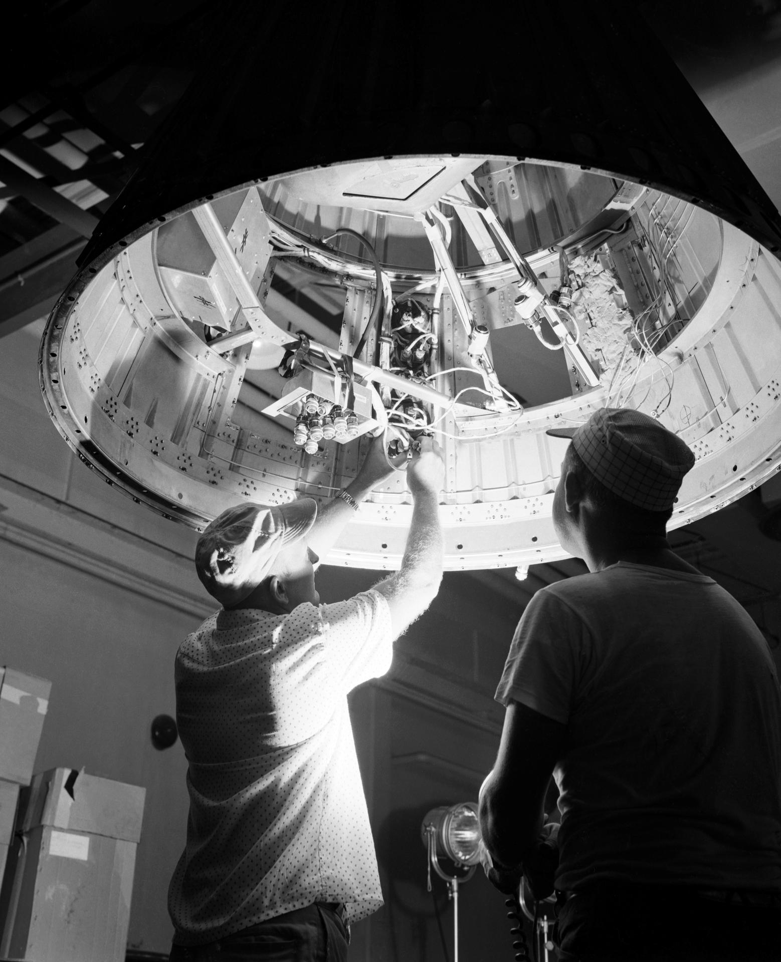 Two men reach up to work on a rocket motor for Project Mercury