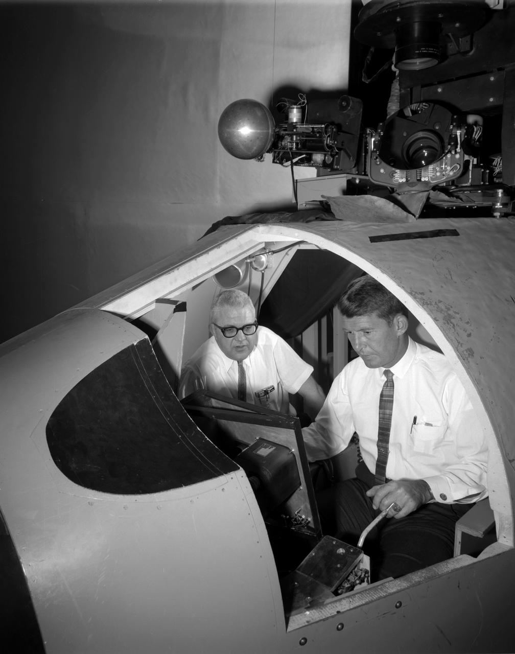 Walter (Wally) M. Schirra in Visual Docking Simulator From A.W. Vogeley, "Piloted Space-Flight Simulation at Langley Research Center," Paper presented at the American Society of Mechanical Engineers 1966 Winter Meeting, New York, NY, November 27-December 1, 1966. "This facility was [later known as the Visual-Optical Simulator. It presents to the pilot an out-the-window view of his target in correct 6 degrees of freedom motion. The scene is obtained by a television camera pick-up viewing a small-scale gimbaled model of the target. "For docking studies, the docking target picture was projected onto the surface of a 20-foot-diameter sphere and the pilot could, effectively, maneuver into contract. this facility was used in a comparison study with the Rendezvous Docking Simulator - one of the few comparison experiments in which conditions were carefully controlled and a reasonable sample of pilots used. All pilots preferred the more realistic RDS visual scene. The pilots generally liked the RDS angular motion cues although some objected to the false gravity cues that these motions introduced. Training time was shorter on the RDS, but final performance on both simulators was essentially equal. " "For station-keeping studies, since close approach is not required, the target was presented to the pilot through a virtual-image system which projects his view to infinity, providing a more realistic effect. In addition to the target, the system also projects a star and horizon background. "