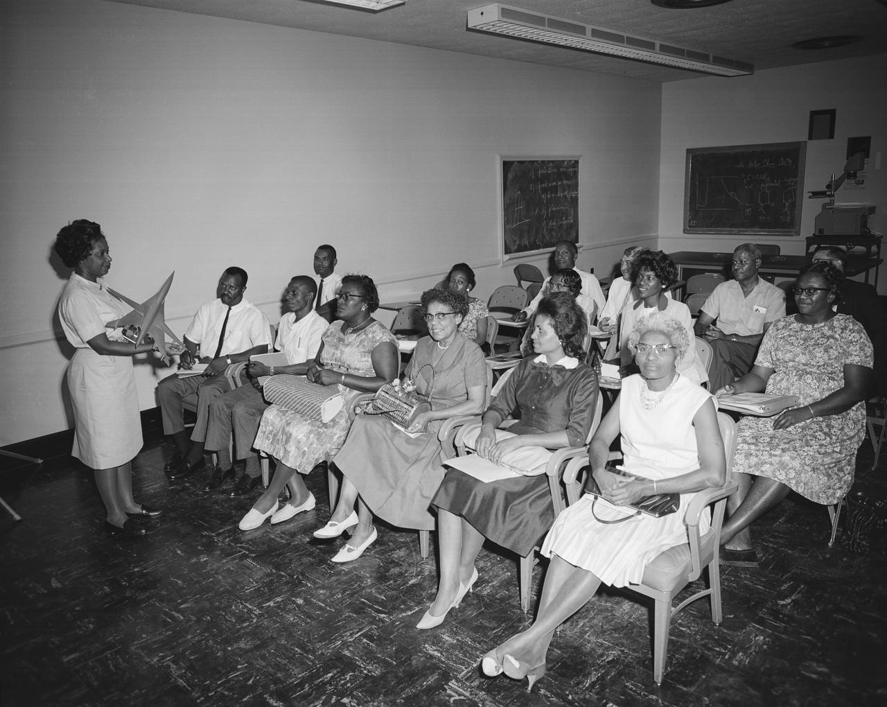 Photograph taken July 30, 1964. Mary W Jackson, Aerospace Engineer in the Large Supersonic Tunnels Branch of Full-Scale Research Division, explains the facilities used in testing research models such as SCAT. The Guidance Counseling Class from Hampton Institute visited the center on July 30 and toured a number of facilities. The purpose of the visit was to provide the counselors an opportunity to see areas of work representing fields in which their students might be employed. The group, under the direction of Professor Fissell Jones (Left, back row) of Hampton Institute, represented the states of Virginia, North Carolina, South Carolina, and Georgia. In 1958 Mary Jackson became NASA's first black female engineer. The Hampton Institute (now Hampton University) is a Historically Black College. NASA started its EEO office in 1964 and the NASA Administrator at the time, James Webb, was very enthusiastic about reaching out to universities (including HBCUs) to partner with them and to encourage students to become NASA engineers.