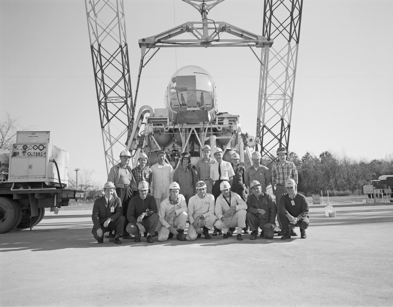 Group photo with crew and Astronaut Roger Chaffee at Lunar Lander Research Facility.  Chaffee was one of the third group of astronauts selected by NASA in October 1963. In addition to participating in the overall training program, he was also tasked with working on flight control communications systems, instrumentation systems, and attitude and translation control systems in the Apollo Branch of the Astronaut office. On March 21, 1966, he was selected as one of the pilots for the AS-204 mission, the first 3-man Apollo flight. Lieutenant Commander Chaffee died on January 27, 1967, in the Apollo spacecraft flash fire during a launch pad test at Kennedy Space Center, Florida.