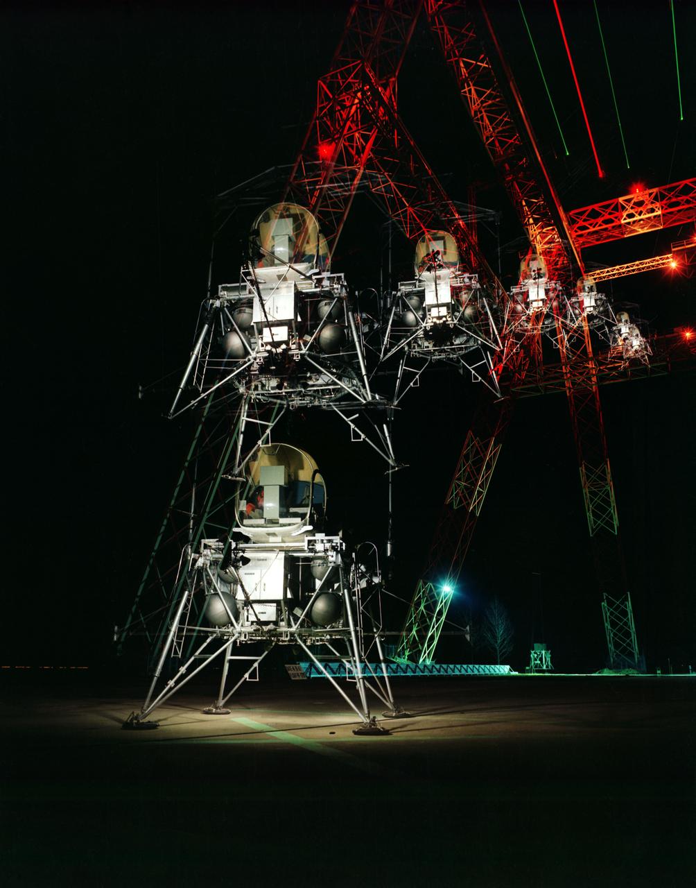 During a nighttime training session, a multiple exposure captures the movement of the Lunar Excursion Module Simulator (LEMS). The LEMS was a manned vehicle used to familiarize the Apollo astronauts with the handling characteristics of lunar-landing type vehicle.  The Apollo Program is best known for the astronaut Neal Armstrong s first step on the Moon July 20, 1969. In its earliest test period, the LEMS featured a helicopter crew cabin atop the lunar landing module. Later, the helicopter crew cabin was replaced with a stand-up rectangular cabin which was more efficient for controlling maneuvers and for better viewing by the pilot.  The vehicle was designed at Langley Research Center in Hampton, VA.  This multiple exposure shows a simulated Moon landing of the (LEMS) trainer at Langley s Lunar Landing Research Facility.  -- Photograph published in Winds of Change, 75th Anniversary NASA publication (page 70), by James Shultz. Also published in  " A Century at Langley" by Joseph Chambers, pg. 93. 