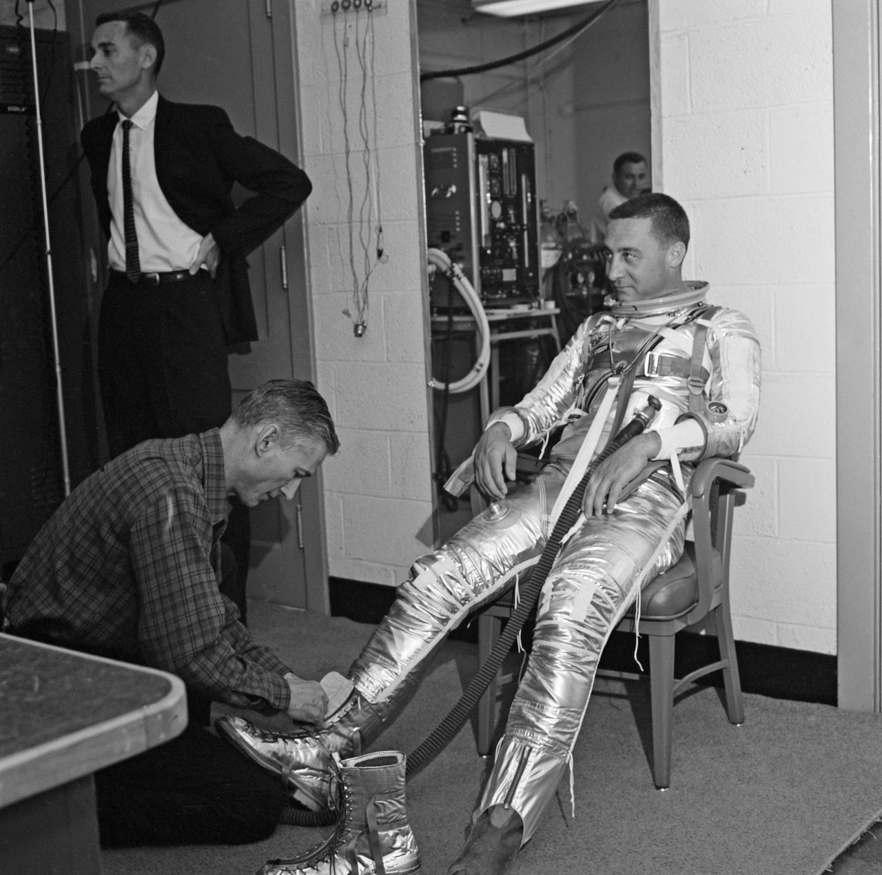 Gus Grissom trying on a Spacesuit; Seated with assistant; Seated with assistant putting on boots; Standing by mirror, name tag visible; Outside in suit, name tag visible. Mercury Project photo, 1961. Original negatives sent to Johnson Space Center when astronauts moved to that center.  Photograph take on 03/27/1961.