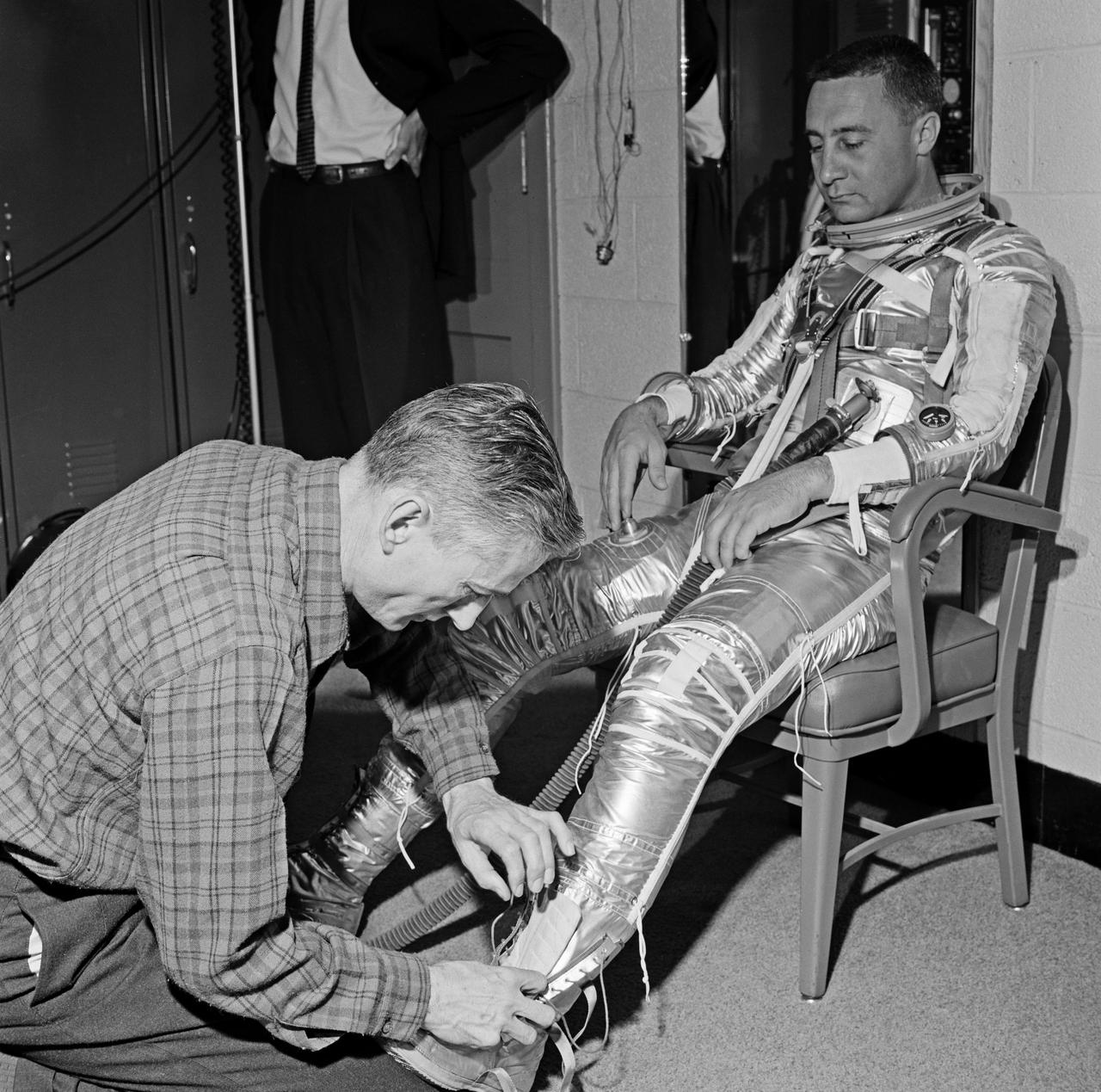 Gus Grissom trying on a Spacesuit; Seated with assistant; Seated with assistant putting on boots; Standing by mirror, name tag visible; Outside in suit, name tag visible. Mercury Project photo, 1961. Original negatives sent to Johnson Space Center when astronauts moved to that center.  Photograph take on 03/27/1961.