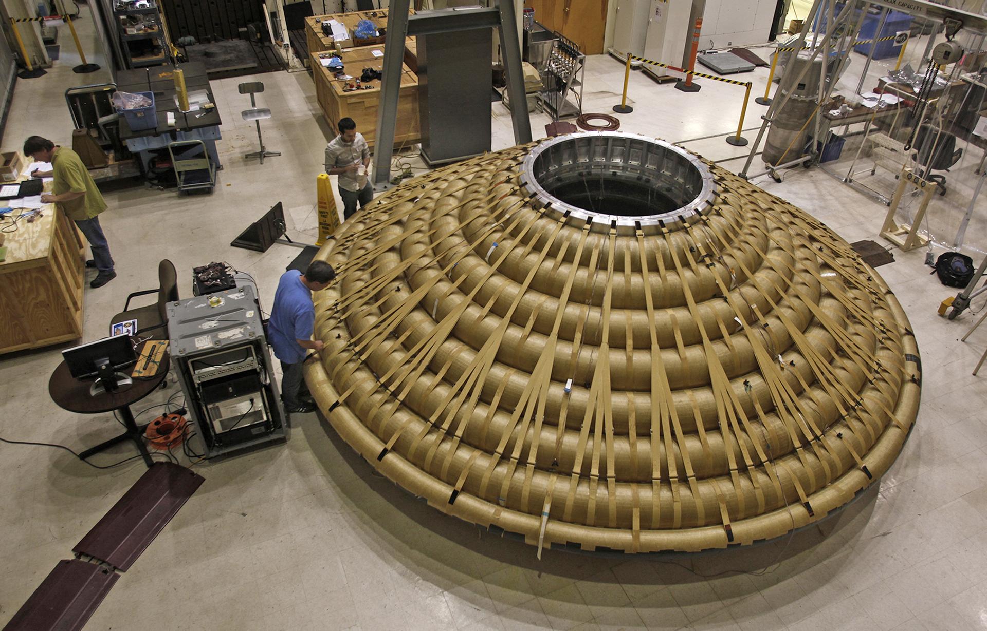 A large woven thermal-protection structure in a lab, made of stacked tan fabric rings.