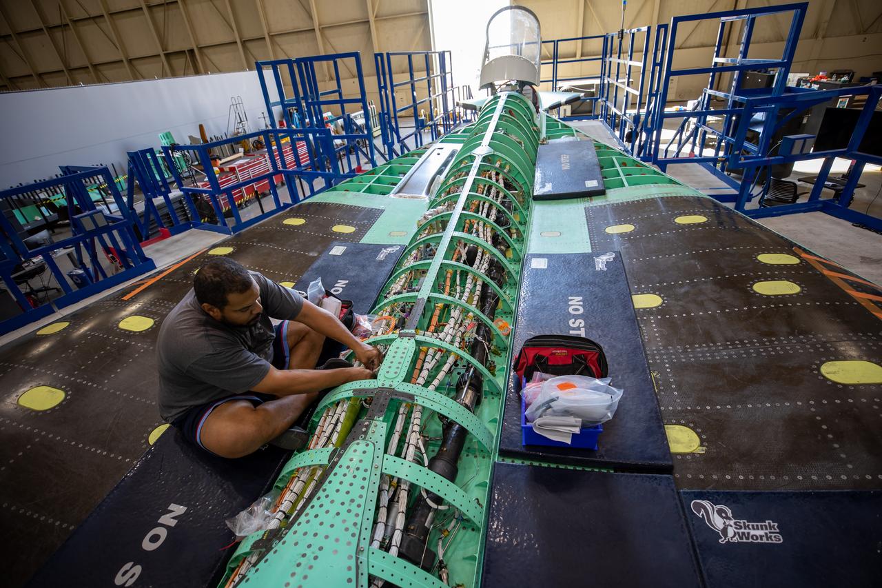A Lockheed Martin technician works to complete wiring on the X-59 aircraft in preparation for the power-on system checkouts.  Once complete, the X-59 aircraft will demonstrate the ability to fly supersonic while reducing the loud sonic boom to a quiet sonic thump and help enable commercial supersonic air travel over land. This aircraft is the centerpiece of NASA’s Quesst mission.