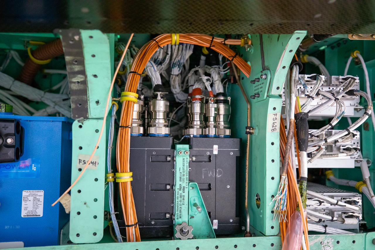 This is a closeup view of the inner workings of the X-59 aircraft. Visible are one the plane’s three lithium-ion batteries (blue box), electrical power system and other wiring components including the vehicle management systems computers (two black boxes) and the white wirings which assist in providing the power that is needed for the aircraft to function in flight.  All of these components are essential to maintaining and monitoring the X-59 once it takes to the skies.  The X-59 is the centerpiece of the Quesst mission which plans to help enable commercial supersonic air travel over land. 