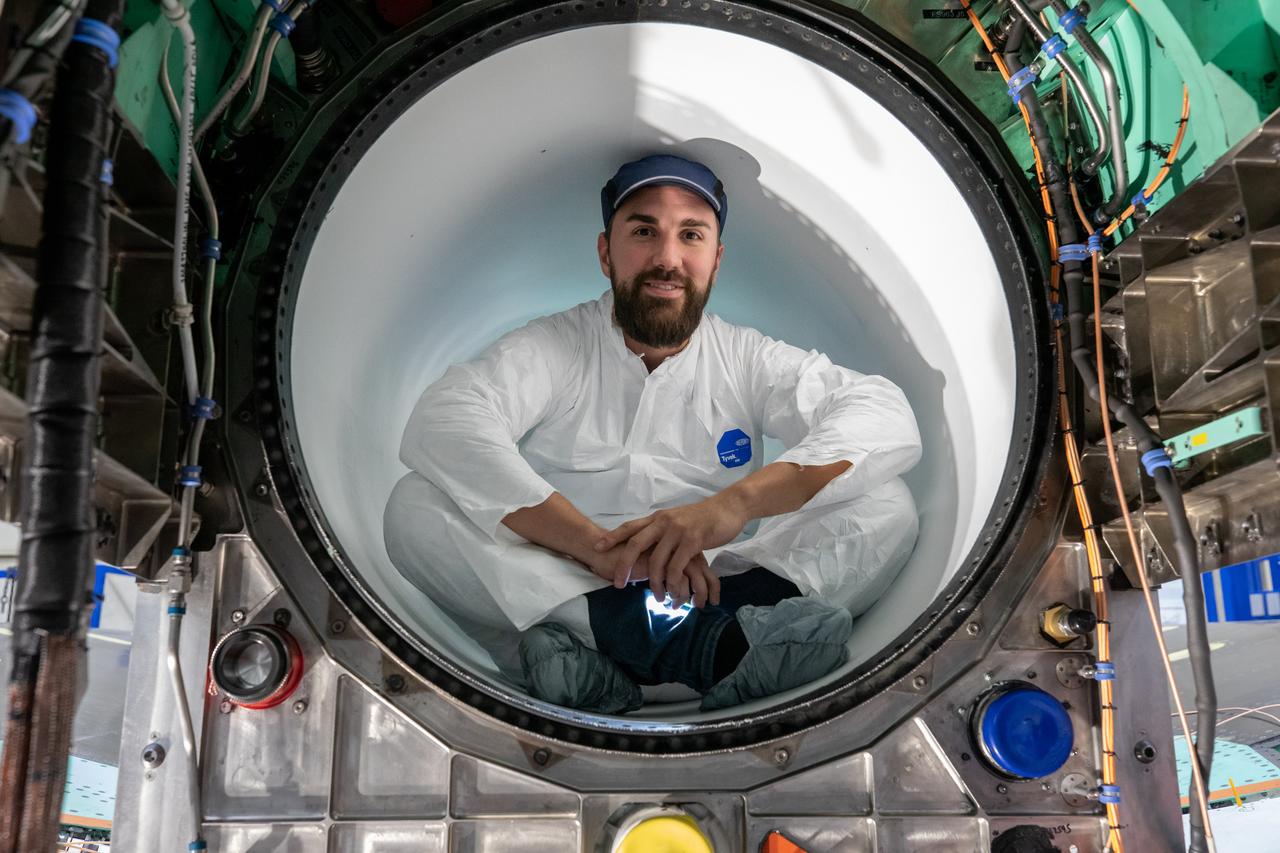 A Lockheed Martin Skunk Works technician takes a break for a photo. Note that the technician is wearing protective clean gear while sitting inside the X-59 engine inlet. Wearing this gear reduces the chance of any foreign objects from damaging the engine inlet.