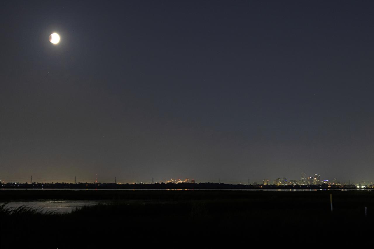 The beginning of the eclipse of the Super Flower Blood Moon over Bayou Bienvenue with the New Orleans Crescent City Connection in the distance early Wednesday morning, May 26, 2021. Image credit: NASA/Michael DeMocker