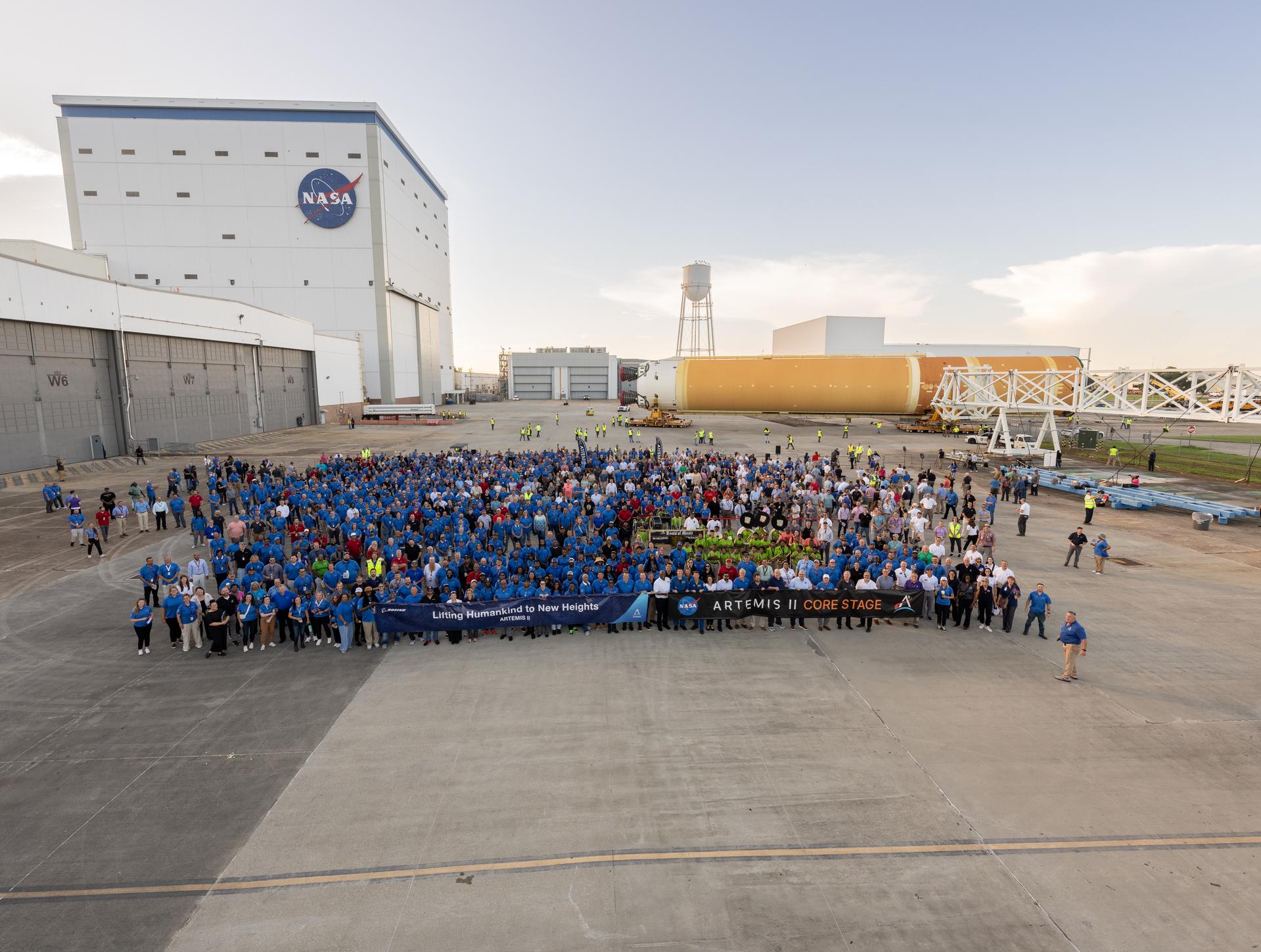 The NASA Michoud Assembly Facility workforce and with other agency team members take a “family photo” with the SLS (Space Launch System) core stage for Artemis II in the background. The core stage will help launch the first crewed flight of NASA’s SLS rocket for the agency’s Artemis II mission. The move marked the first time a fully assembled Moon rocket stage for a crewed mission has rolled out from NASA’s Michoud Assembly Facility in New Orleans since the Apollo Program, The core stage was moved onto the agency’s Pegasus barge, where it will be ferried to NASA’s Kennedy Space Center in Florida.  The core stage for the SLS mega rocket is the largest stage NASA has ever produced. At 212 feet tall, the stage consists of five major elements, including two huge propellant tanks that collectively hold more than 733,000 gallons of super chilled liquid propellant to feed four RS-25 engines at its base. During launch and flight, the stage will operate for just over eight minutes, producing more than 2 million pounds of thrust to help send a crew of four astronauts inside NASA’s Orion spacecraft onward to the Moon.  NASA is working to land the first woman, first person of color, and its first international partner astronaut on the Moon under Artemis. SLS is part of NASA’s backbone for deep space exploration, along with the Orion spacecraft and Gateway in orbit around the Moon and commercial human landing systems, next-generation space, next-generational spacesuits, and rovers on the lunar surface. SLS is the only rocket that can send Orion, astronauts, and supplies to the Moon in a single launch.