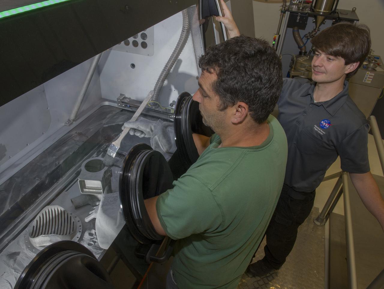 JIM LYDON (LEFT-GREEN SHIRT) BRUSHES METALLIC POWDER OFF OF A RECENTLY PRINTED ROCKET PART EXAMINED BY ZACH JONES, RIGHT, IN MSFC'S ADDITIVE MANUFACTURING LAB