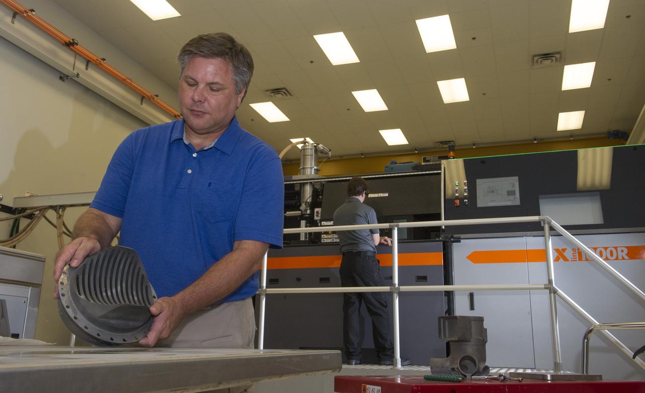 ANDY HARDIN, A PROPULSION ENGINEER AT NASA'S MARSHALL SPACE FLIGHT CENTER IN HUNTSVILLE, ALABAMA, SHOWS A 3-D PRINTED ROCKET PART MADE WITH A SELECTIVE LASER MELTING MACHINE. PARTS FOR THE SPACE LAUNCH SYSTEM'S RS-25 ROCKET ENGINE ARE BEING MADE WITH THE MACHINE IN THE BACKGROUND