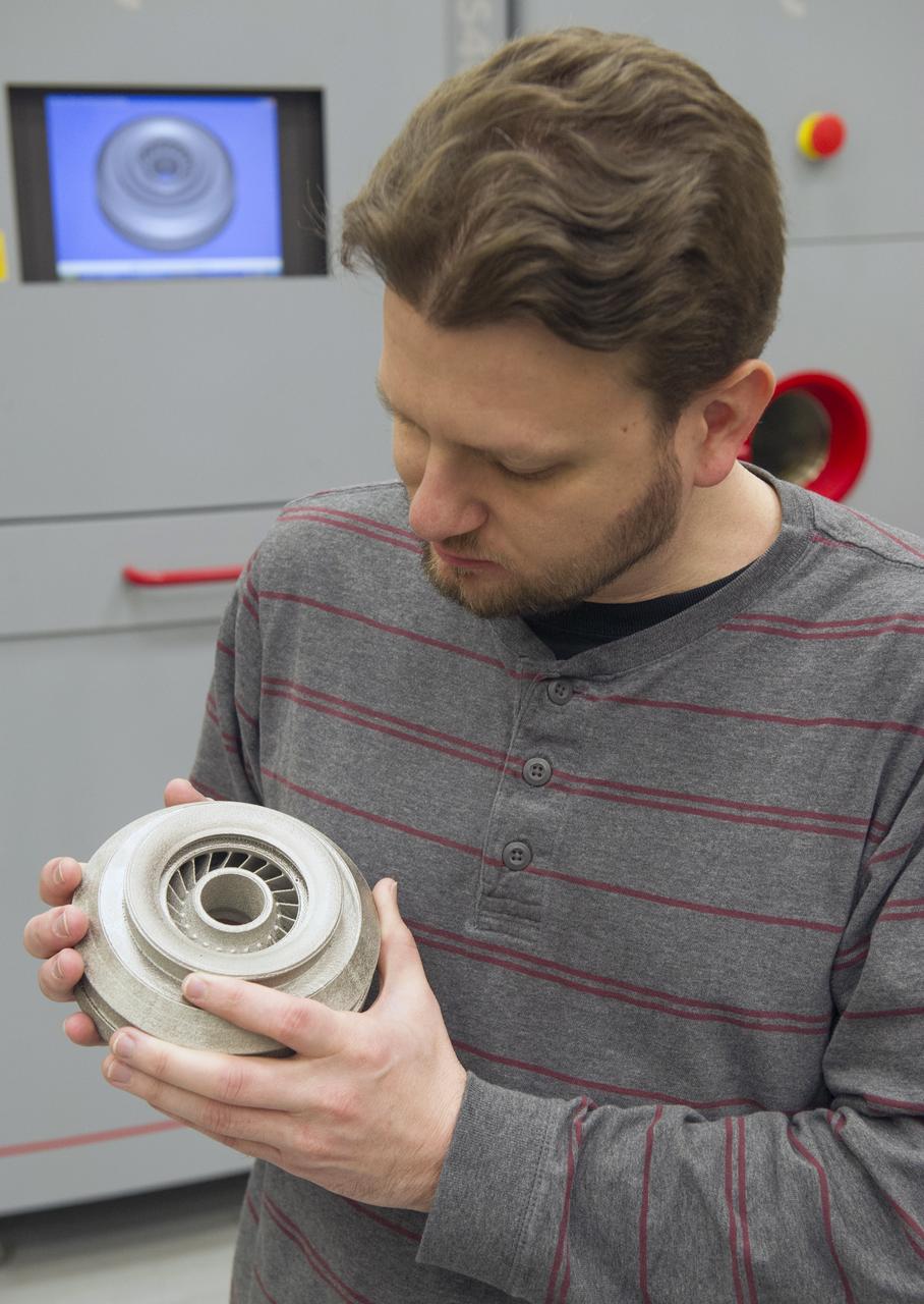 QUINCY BEAN OF MSFC’S ADVANCED MANUFACTURING TEAM, WITH TITANIUM ALLOY TURBOPUMP COMPONENT FABRICATED WITH MSFC’S ELECTRON BEAM MELTING SYSTEM (BACKGROUND).