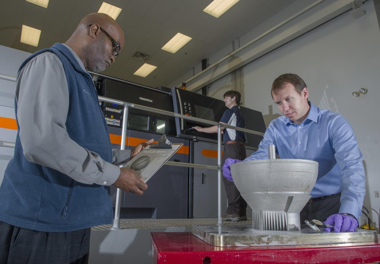 JOHNNIE CLARK, BRIAN WEST, AND ZACK JONES OF MSFC’S ADVANCED MANUFACTURING TEAM, WITH MSFC’S XLINE SELECTIVE LASER MELTING SYSTEM.  CURRENTLY ONE OF THE LARGEST METAL 3D PRINTERS, THE XLINE AT MARSHALL IS BEING USED TO DEVELOP AND CERTIFY NICKEL ALLOY 718 MATERIAL PROPERTIES AND LARGE MANUFACTURING TECH DEMOS FOR THE RS25 ENGINE AND THE COMMERCIAL CREWED VEHICLE PROJECTS.