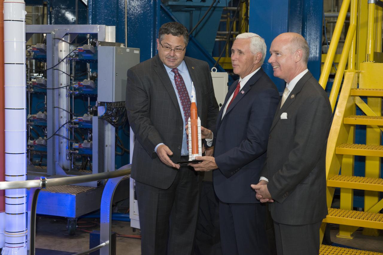 Marshall Space Flight Center Director Todd May (left) presents Vice President Mike Pence (center) with a Space Launch System model.  May, Vice President Pence, and Congressman Robert Aderholt (R-AL) (right) are standing in front of an SLS test stand where the engine section, the bottom section of the 212-foot-tall core stage, is being tested.  Earlier, engineers working on the test gave the Vice President a close up look at test hardware. The test hardware is for the SLS core stage engine section, which is the bottom of the core stage where the four RS-25 engines are housed. The engine section structure must withstand the incredible stresses produced by more than 8 million pounds of thrust during launch and ascent. 
