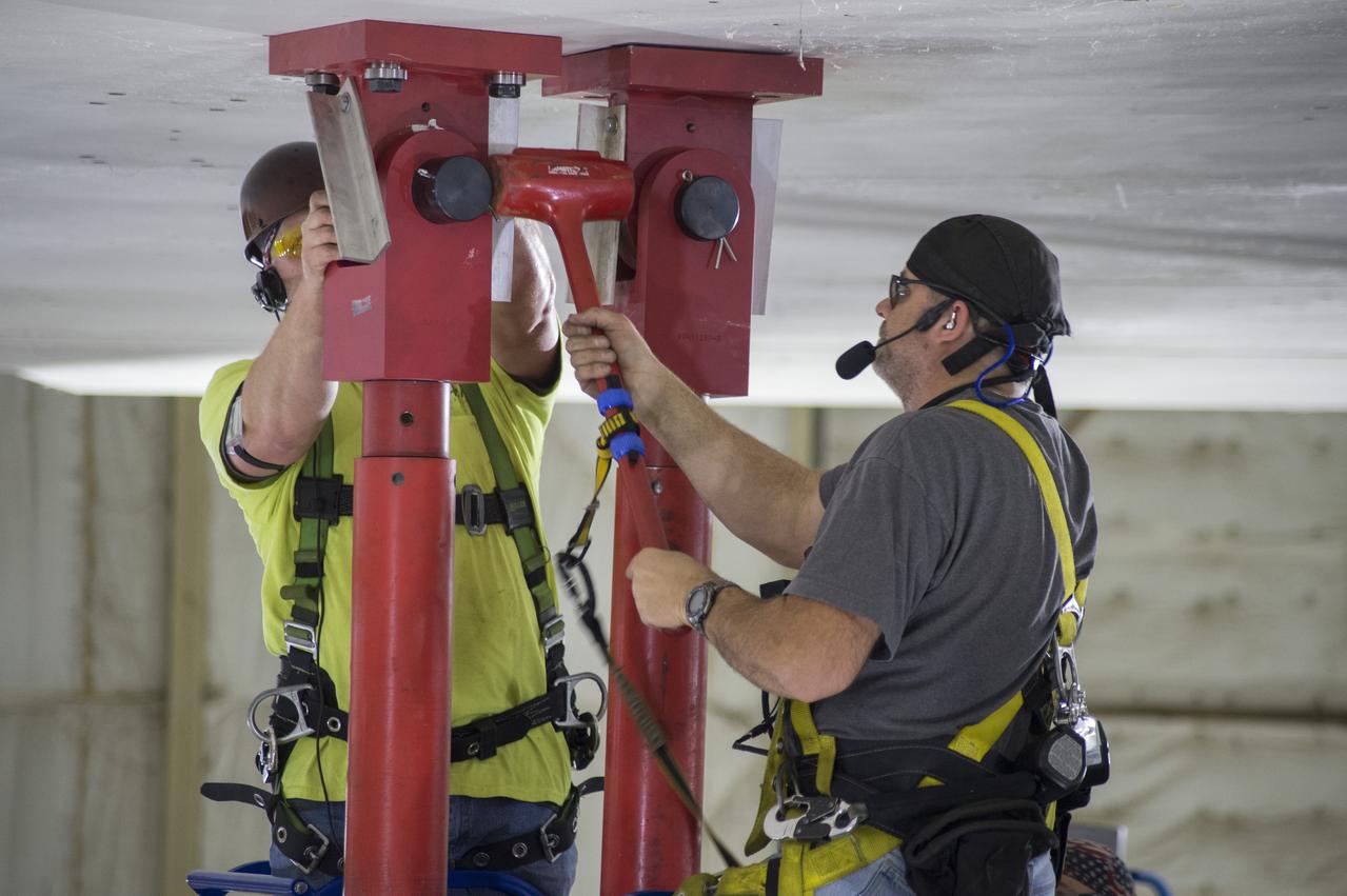 SLS Intertank Test Article, ITA, is attached to crosshead of load test Annex, Bldg. 4619, and removed from bed of KMAG transporter.  Rob Ziegler, (L), and Roger Myrick (R), of Aerie Aerospace attach load lines to Aft Load Ring of Intertank Test Article.