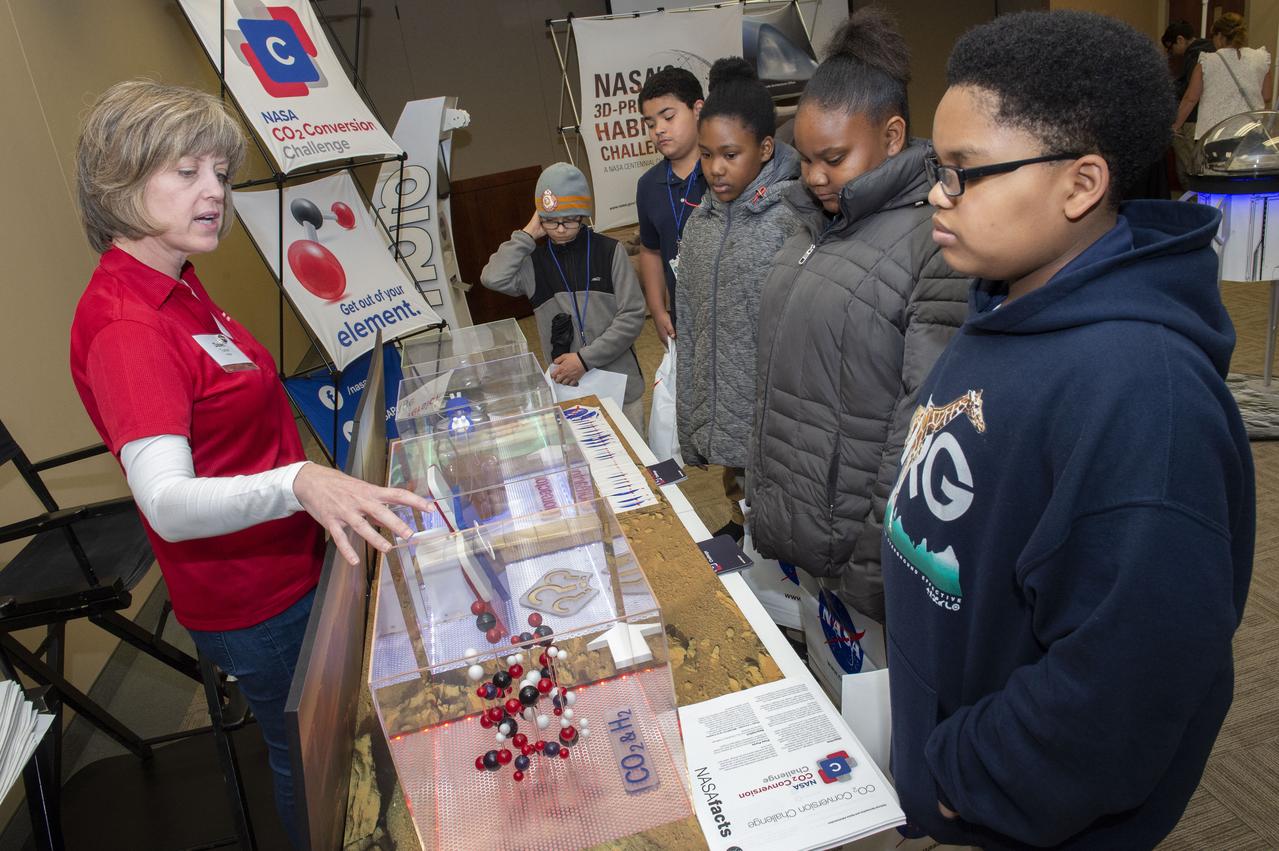 AI. SpaceFactory of New York and Pennsylvania State University of College Park print subscale habitat structures at NASA's 3D-Printed Habitat Challenge, held at the Caterpillar Edwards Demonstration & Learning Center in Edwards, Illinois, May 1-4, 2019. The habitat print is the final level of the multi-phase competition, which began in in 2015. The challenge is managed by NASA's Centennial Challenges program, and partner Bradley University of Peoria, Illinois.  Dawn Mercer Turner talks to school children about CO2 conversion.