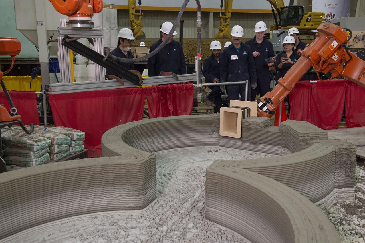 AI. SpaceFactory of New York and Pennsylvania State University of College Park print subscale habitat structures at NASA's 3D-Printed Habitat Challenge, held at the Caterpillar Edwards Demonstration & Learning Center in Edwards, Illinois, May 1-4, 2019. The habitat print is the final level of the multi-phase competition, which began in in 2015. The challenge is managed by NASA's Centennial Challenges program, and partner Bradley University of Peoria, Illinois.  Insertion of window element in Penn State Habitat. 