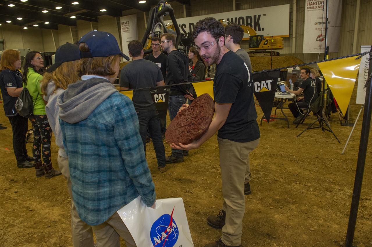 AI. SpaceFactory of New York and Pennsylvania State University of College Park print subscale habitat structures at NASA's 3D-Printed Habitat Challenge, held at the Caterpillar Edwards Demonstration & Learning Center in Edwards, Illinois, May 1-4, 2019. The habitat print is the final level of the multi-phase competition, which began in in 2015. The challenge is managed by NASA's Centennial Challenges program, and partner Bradley University of Peoria, Illinois.  AI team member shows early unsuccessful attempt at printing to students viewing the competition.