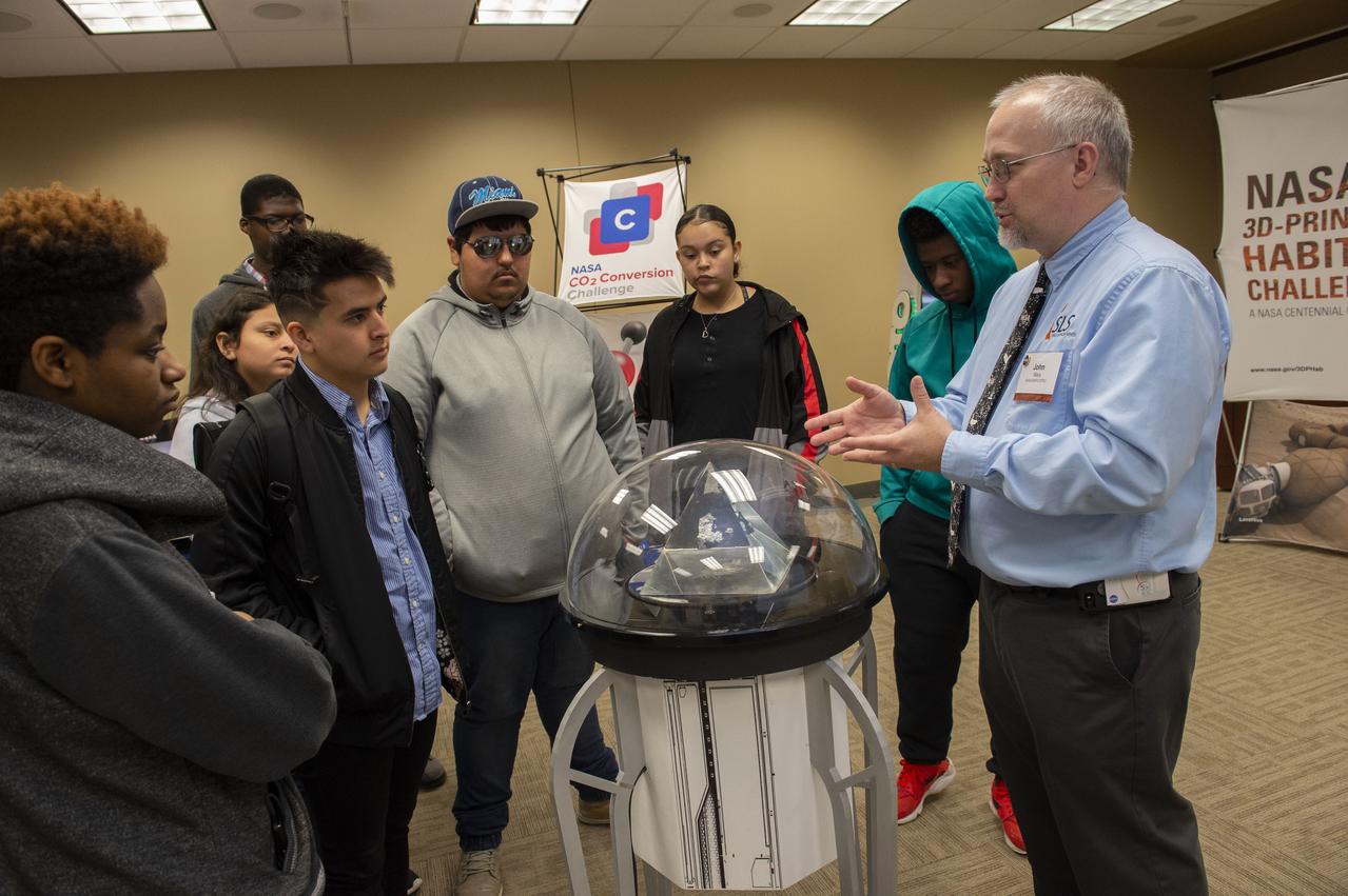 AI. SpaceFactory of New York and Pennsylvania State University of College Park print subscale habitat structures at NASA's 3D-Printed Habitat Challenge, held at the Caterpillar Edwards Demonstration & Learning Center in Edwards, Illinois, May 1-4, 2019. The habitat print is the final level of the multi-phase competition, which began in in 2015. The challenge is managed by NASA's Centennial Challenges program, and partner Bradley University of Peoria, Illinois.  Marshall Space Flight Center educator john Weis, right, offers students from Manual Academic High School in Peoria, Illinois a first-hand look at a Moon rock retrieved by the Apollo 15 mission.