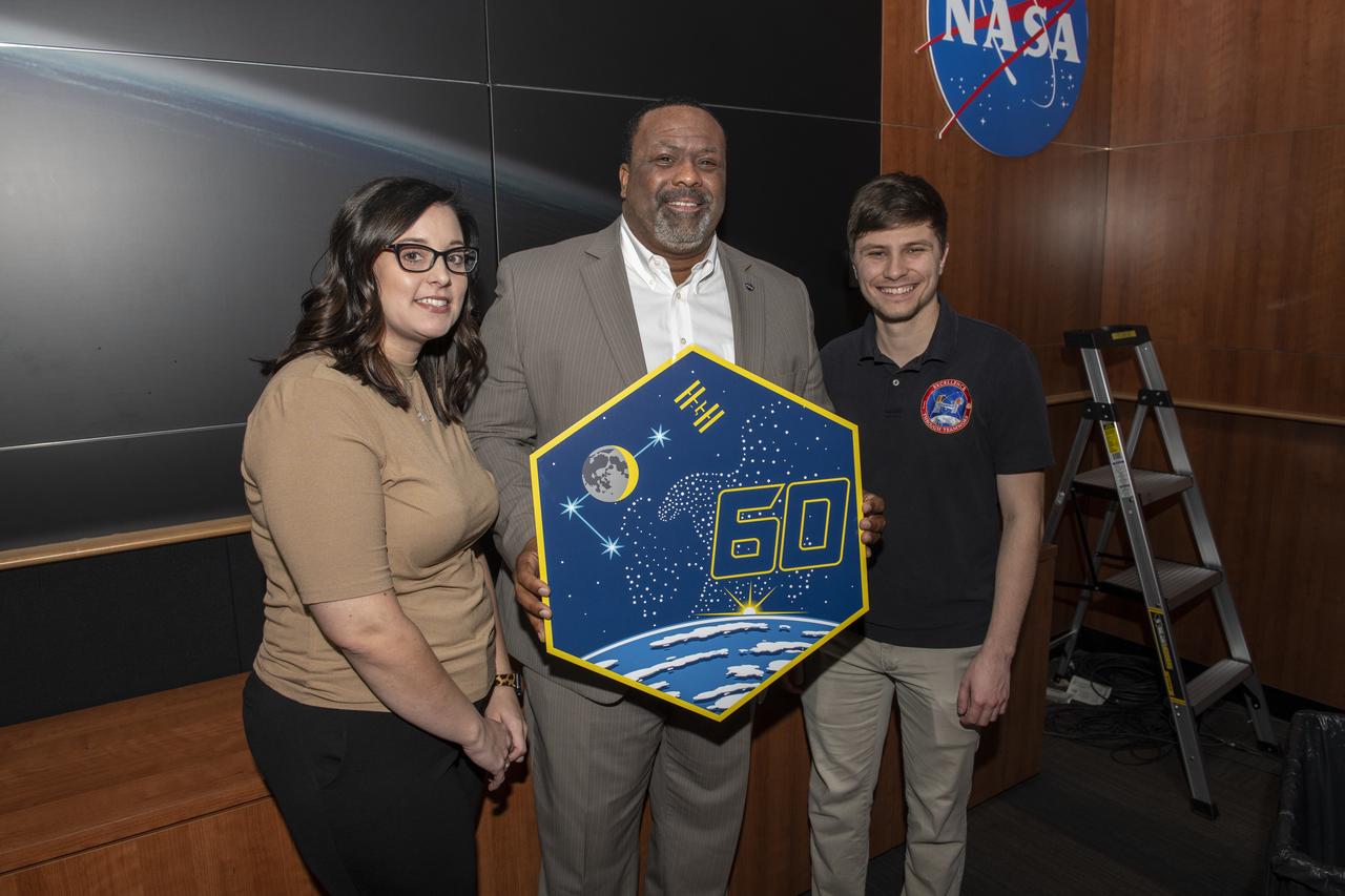 Increment 60 plaque hanging in the Payload Operations Operation Integration (POC) facility.  Dwight Mosby holding the Increment 60 plaque along with Kira Thomas and Christian Bonner who hung the plaque.