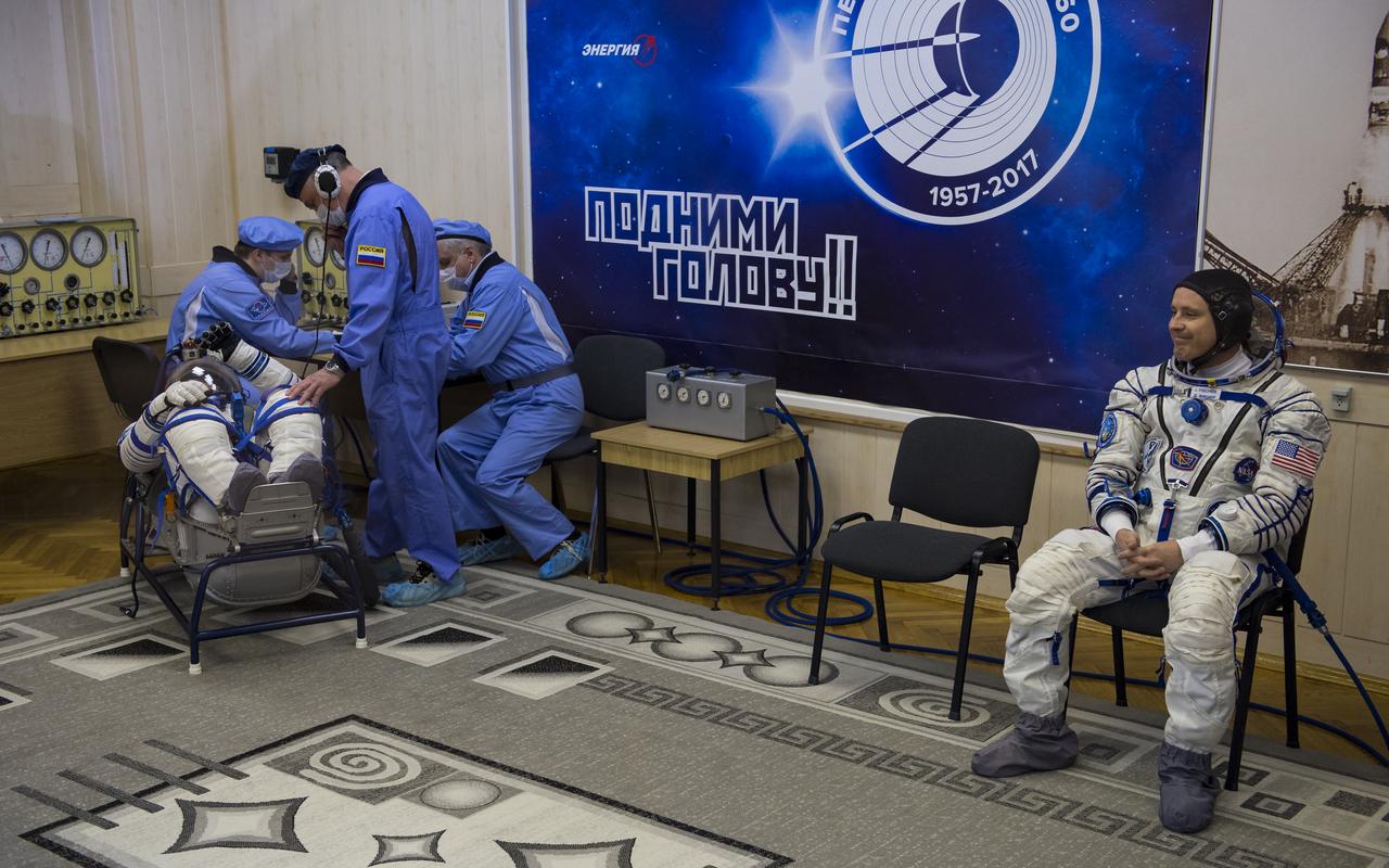 Expedition 51 Flight Engineer Jack Fischer of NASA smiles at friends and family while his crewmate Soyuz Commander Fyodor Yurchikhin of Roscosmos has his Russian Sokol suit pressure checked in preparation for launch aboard the Soyuz MS-04 spacecraft on Thursday, April 20, 2017 at the Baikonur Cosmodrome in Kazakhstan. Launch of the Soyuz rocket is scheduled for 1:13pm April 20 Baikonur time, and will carry Fischer and Yurchikhin into orbit to begin their four and a half month mission on the International Space Station. Photo Credit: (NASA/Aubrey Gemignani)