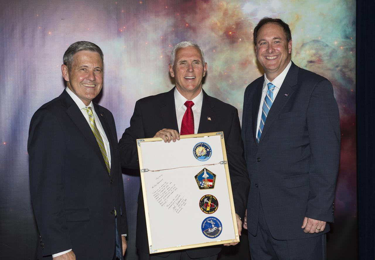 Vice President Mike Pence receives a commemorative montage from Kennedy Space Center (KSC) Director, Robert Cabana, left, and Acting NASA Administrator, Robert Lightfoot, right, including stickers on the back from all of Cabana's missions, Thursday, July 6, 2017, in the green room at KSC in Cape Canaveral, Florida. Vice President Mike Pence is scheduled to speak at the event to highlight innovations made in America and tour some of the public/private partnership work that is helping to transform the center into a multi-user spaceport. Photo Credit: (NASA/Aubrey Gemignani)
