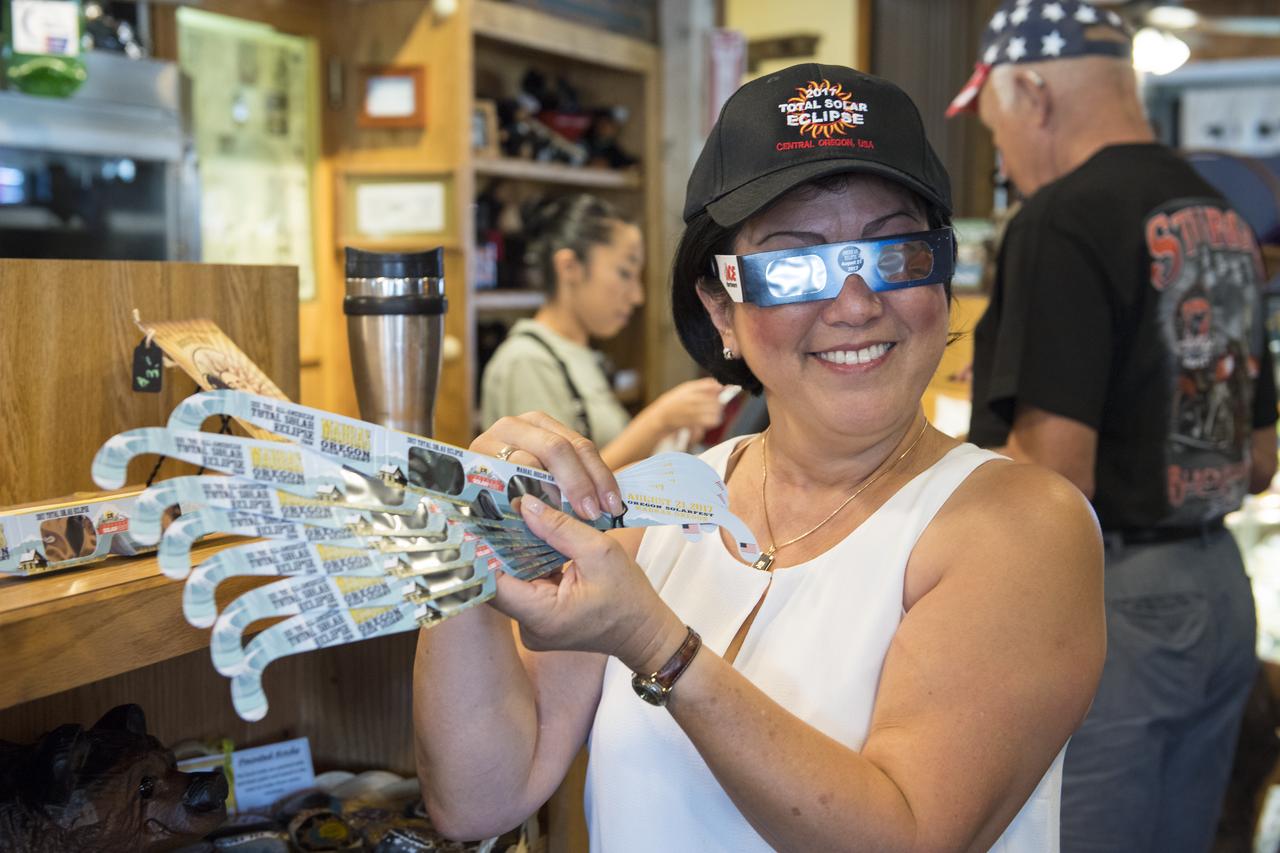 Carol Jensen, a produce purveyor for Black Bear Diner, is seen displaying solar glasses for sale at Black Bear Diner in Madras, Oregon on Saturday, August 19, 2017. She is volunteering her time to help prepare for the crowds arriving to watch the total solar eclipse. The eclipse will be sweeping across a narrow portion of the contiguous United States from Lincoln Beach, Oregon to Charleston, South Carolina on August 21. A partial solar eclipse will be visible across the entire North American continent along with parts of South America, Africa, and Europe.  Photo Credit: (NASA/Aubrey Gemignani)