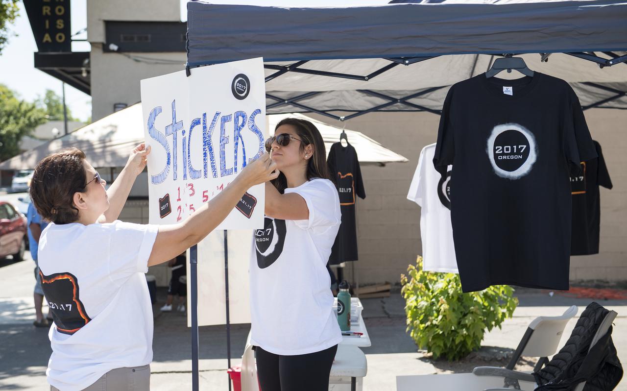 Lili Bornio, right, and her mom, set up to sell eclipse shirts and stickers, that she designed, to raise money for medical school, in Madras, Oregon on Saturday, August 19, 2017. Thousands of visitors are expected in Madras to view the total solar eclipse. The eclipse will be sweeping across a narrow portion of the contiguous United States from Lincoln Beach, Oregon to Charleston, South Carolina on August 21. A partial solar eclipse will be visible across the entire North American continent along with parts of South America, Africa, and Europe.  Photo Credit: (NASA/Aubrey Gemignani)