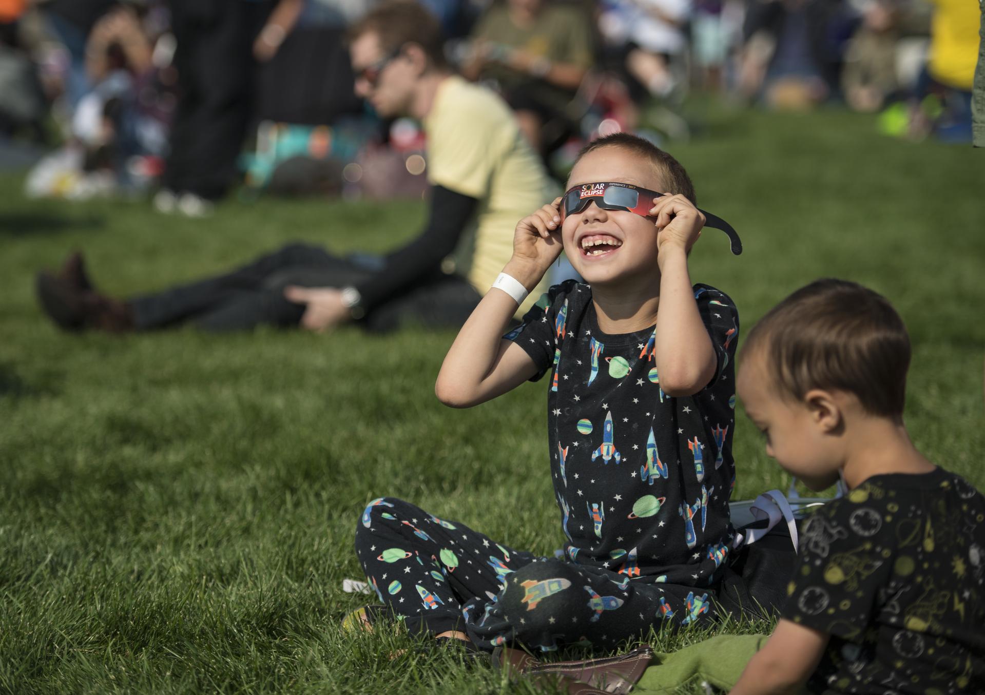 A young child holds eclipse glasses up to their eyes