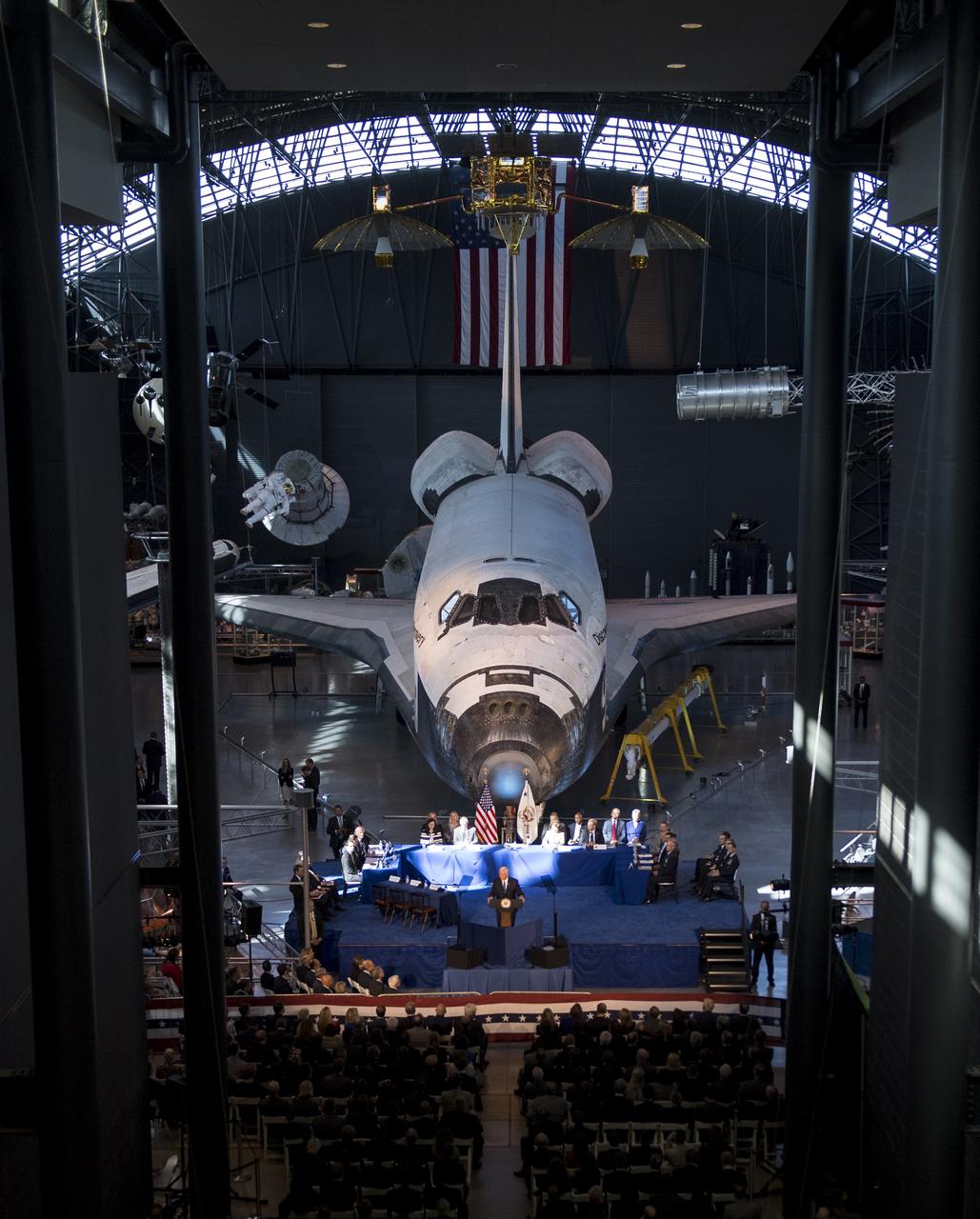 Space shuttle Discovery is seen behind Vice President Mike Pence as he delivers opening remarks during the National Space Council's first meeting, Thursday, Oct. 5, 2017 at the Smithsonian National Air and Space Museum's Steven F. Udvar-Hazy Center in Chantilly, Va. The National Space Council, chaired by Vice President Mike Pence heard testimony from representatives from civil space, commercial space, and national security space industry representatives.  Photo Credit: (NASA/Joel Kowsky)