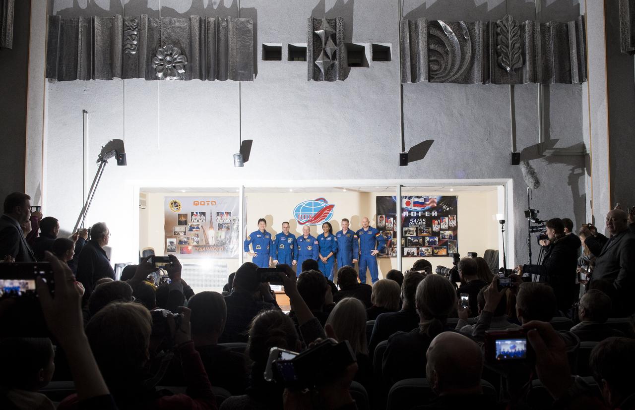 Expedition 54 prime crew members flight engineer Norishige Kanai of the Japan Aerospace Exploration Agency (JAXA), left, Soyuz Commander Anton Shkaplerov of Roscosmos, second from left, flight engineer Scott Tingle of NASA, third from left, pose for a picture with backup crew members Jeanette Epps of NASA, third from right,  Sergey Prokopev of Roscosmos, second from right, and Alex Gerst of ESA (European Space Agency), right, at the conclusion of a press conference, Saturday, Dec. 16, 2017 at the Cosmonaut Hotel in Baikonur, Kazakhstan. Expedition 54 Soyuz Commander Anton Shkaplerov of Roscosmos, flight engineer Scott Tingle of NASA, and flight engineer Norishige Kanai of Japan Aerospace Exploration Agency (JAXA) are scheduled to launch to the International Space Station aboard the Soyuz spacecraft from the Baikonur Cosmodrome on December 17.  Photo Credit: (NASA/Joel Kowsky)