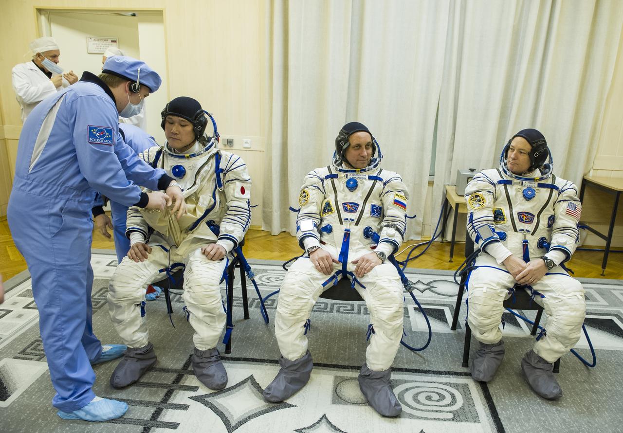 Expedition 54 flight engineer Norishige Kanai of Japan Aerospace Exploration Agency (JAXA), left, is helped into his Russian Sokol suit as he and fellow cremates, Soyuz Commander Anton Shkaplerov of Roscosmos, center, and flight engineer Scott Tingle of NASA, right, prepare for their Soyuz launch to the International Space Station Sunday, Dec. 17, 2017 in Baikonur, Kazakhstan.  Launch of the Soyuz rocket will send Tingle, Kanai, and Shkaplerov on a five month mission aboard the International Space Station. Photo Credit: (NASA/GCTC/Andrey Shelepin)