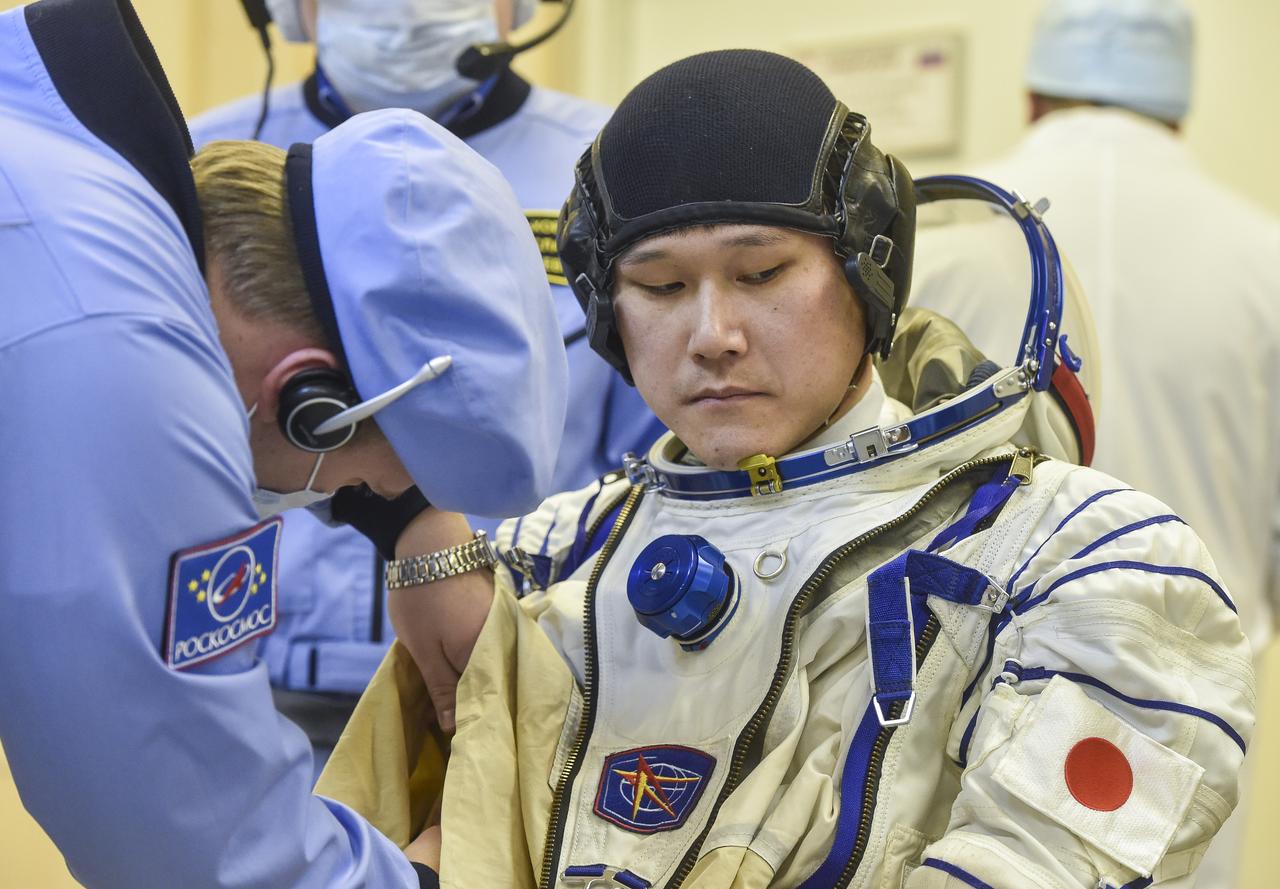 Expedition 54 flight engineer Norishige Kanai of the Japan Aerospace Exploration Agency (JAXA), is helped into his Russian Sokol suit as he and fellow cremates, Soyuz Commander Anton Shkaplerov of Roscosmos, and flight engineer Scott Tingle of NASA, prepare for their Soyuz launch to the International Space Station Sunday, Dec. 17, 2017 in Baikonur, Kazakhstan.  Launch of the Soyuz rocket will send Tingle, Kanai, and Shkaplerov on a five month mission aboard the International Space Station. Photo Credit: (NASA/GCTC/Andrey Shelepin)