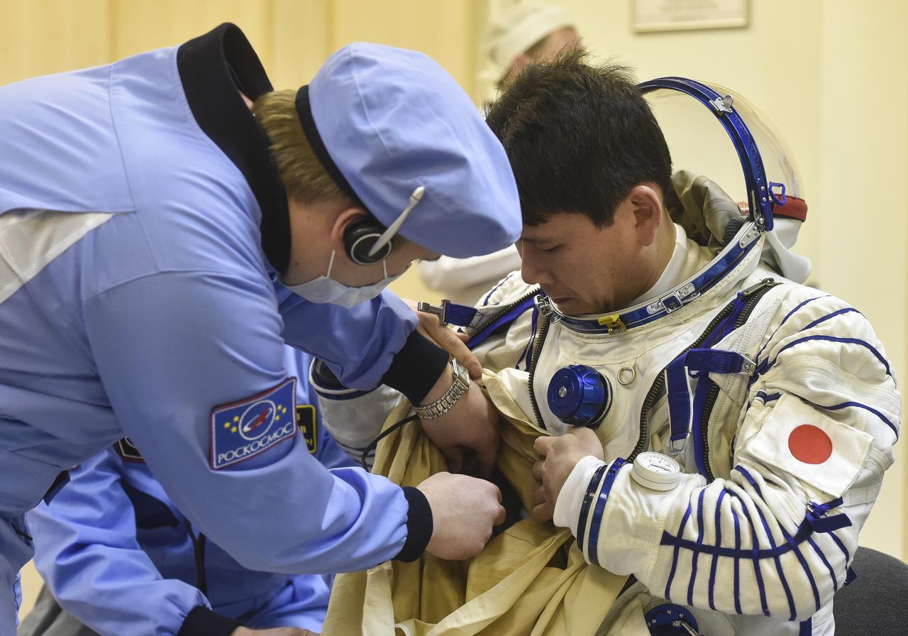 Expedition 54 flight engineer Norishige Kanai of the Japan Aerospace Exploration Agency (JAXA), left, is helped into his Russian Sokol suit as he and fellow cremates, Soyuz Commander Anton Shkaplerov of Roscosmos, center, and flight engineer Scott Tingle of NASA, right, prepare for their Soyuz launch to the International Space Station Sunday, Dec. 17, 2017 in Baikonur, Kazakhstan.  Launch of the Soyuz rocket will send Tingle, Kanai, and Shkaplerov on a five month mission aboard the International Space Station. Photo Credit: (NASA/GCTC/Andrey Shelepin)