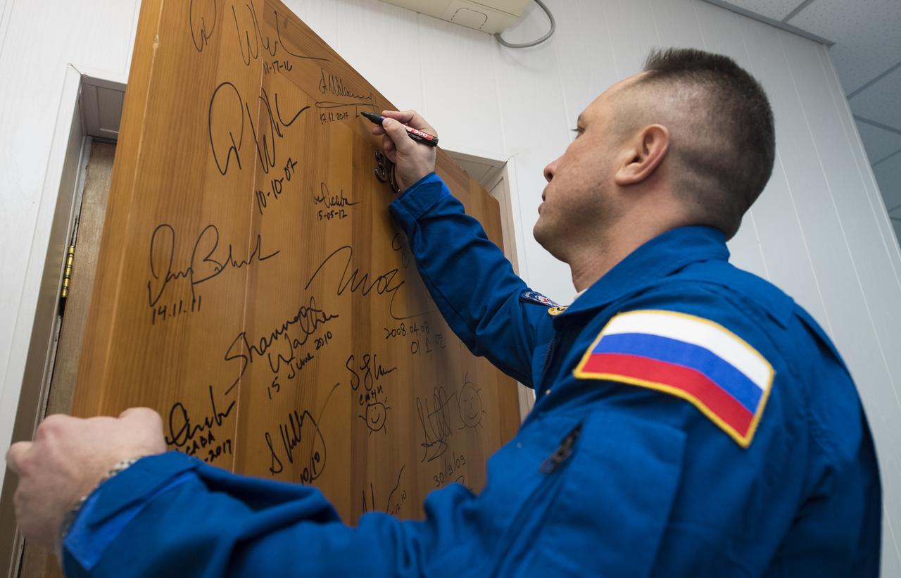 Expedition 54 Soyuz Commander Anton Shkaplerov of Roscosmos performs the traditional door signing at the Cosmonaut Hotel prior to departing the hotel for launch on a Soyuz rocket with fellow cremates flight engineer Norishige Kanai of Japan Aerospace Exploration Agency (JAXA) and flight engineer Scott Tingle of NASA, Sunday, Dec. 17, 2017 in Baikonur, Kazakhstan. Shkaplerov, Tingle, and Kanai will launch in their Soyuz MS-07 to the International Space Station to begin a five month mission. Photo Credit: (NASA/Joel Kowsky)