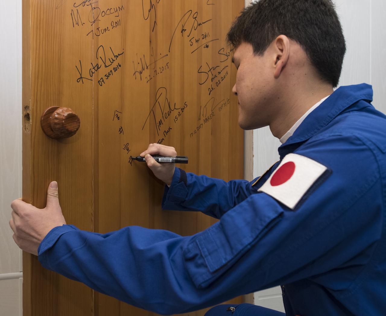 Expedition 54 flight engineer Norishige Kanai of the Japan Aerospace Exploration Agency (JAXA) performs the traditional door signing at the Cosmonaut Hotel prior to departing the hotel for launch on a Soyuz rocket with fellow cremates flight engineer Norishige Kanai of Japan Aerospace Exploration Agency (JAXA) and flight engineer Scott Tingle of NASA, Sunday, Dec. 17, 2017 in Baikonur, Kazakhstan. Kanai, Shkaplerov, and Tingle will launch in their Soyuz MS-07 to the International Space Station to begin a five month mission. Photo Credit: (NASA/Joel Kowsky)