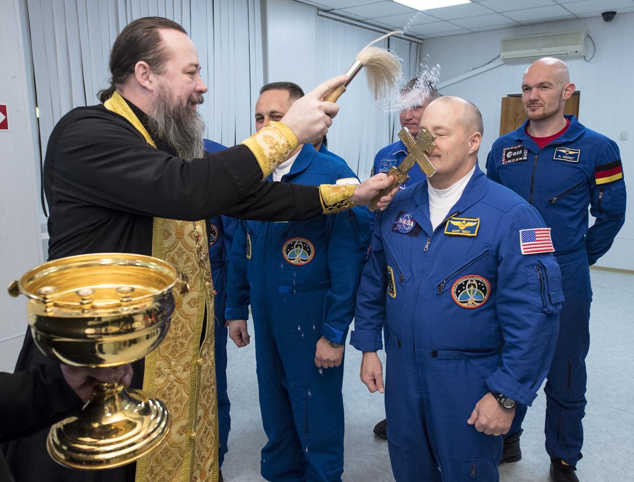 Expedition 54 flight engineer Scott Tingle of NASA receives the traditional blessing from a Russian Orthodox Priest at the Cosmonaut Hotel prior to his launch aboard the Soyuz MS-07 spacecraft to the International Space Station, Sunday, Dec. 17, 2017 in Baikonur, Kazakhstan.  Tingle, Soyuz Commander Anton Shkaplerov of Roscosmos, and flight engineer Norishige Kanai of the Japan Aerospace Exploration Agency (JAXA) will spend the next five months living and working onboard the International Space Station.  Photo Credit: (NASA/Joel Kowsky)