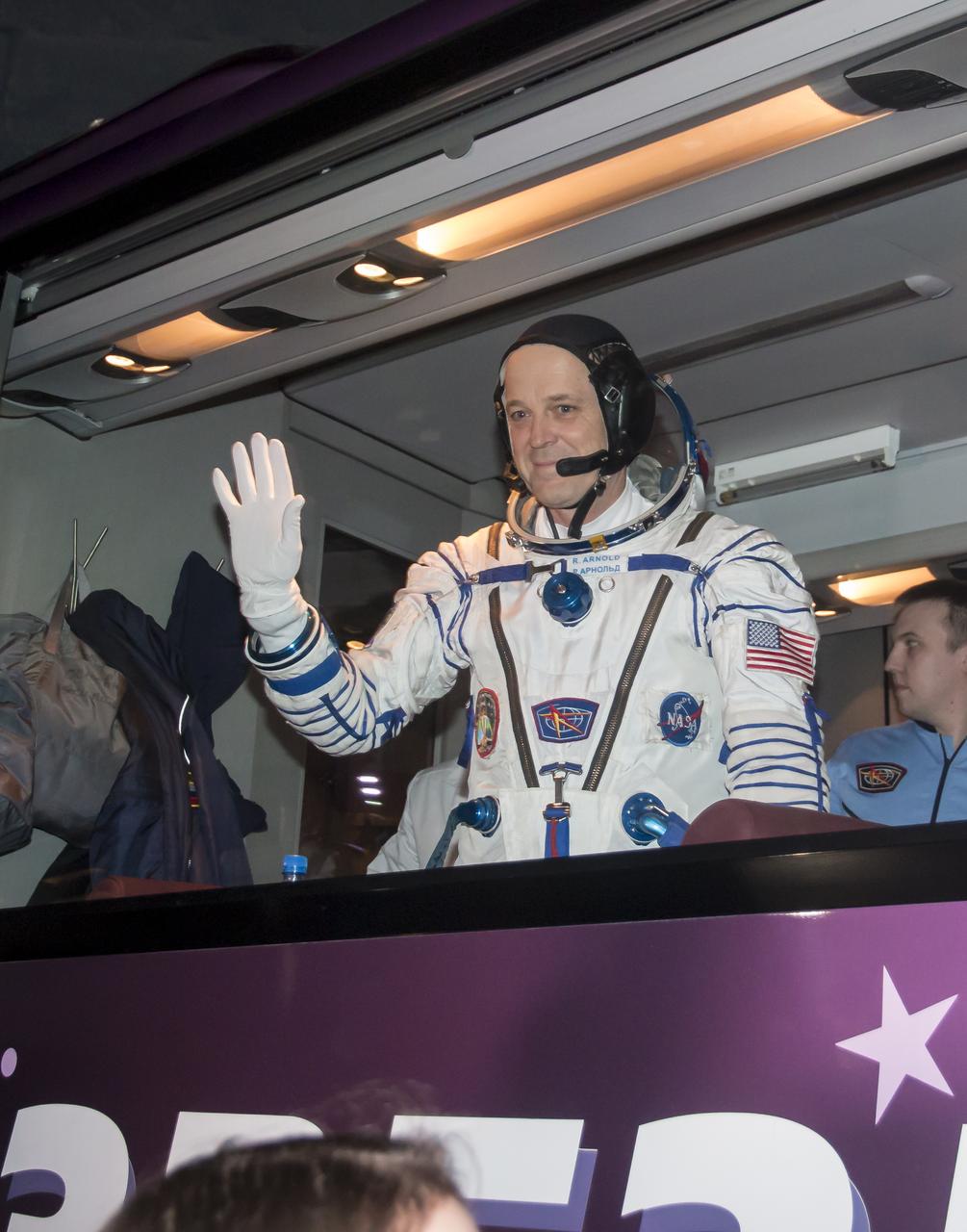 Expedition 55 flight engineer Ricky Arnold of NASA waves farewell as he and Soyuz Commander Oleg Artemyev of Roscosmos and flight engineer Drew Feustel of NASA depart Building 254 for the launch pad a few hours before their launch, Wednesday, March 21, 2018 at the Baikonur Cosmodrome Kazakhstan. Launch of the Soyuz rocket will send Arnold, Artemyev, and Feustel on a five month mission aboard the International Space Station. Photo Credit: (NASA/Victor Zelentsov)