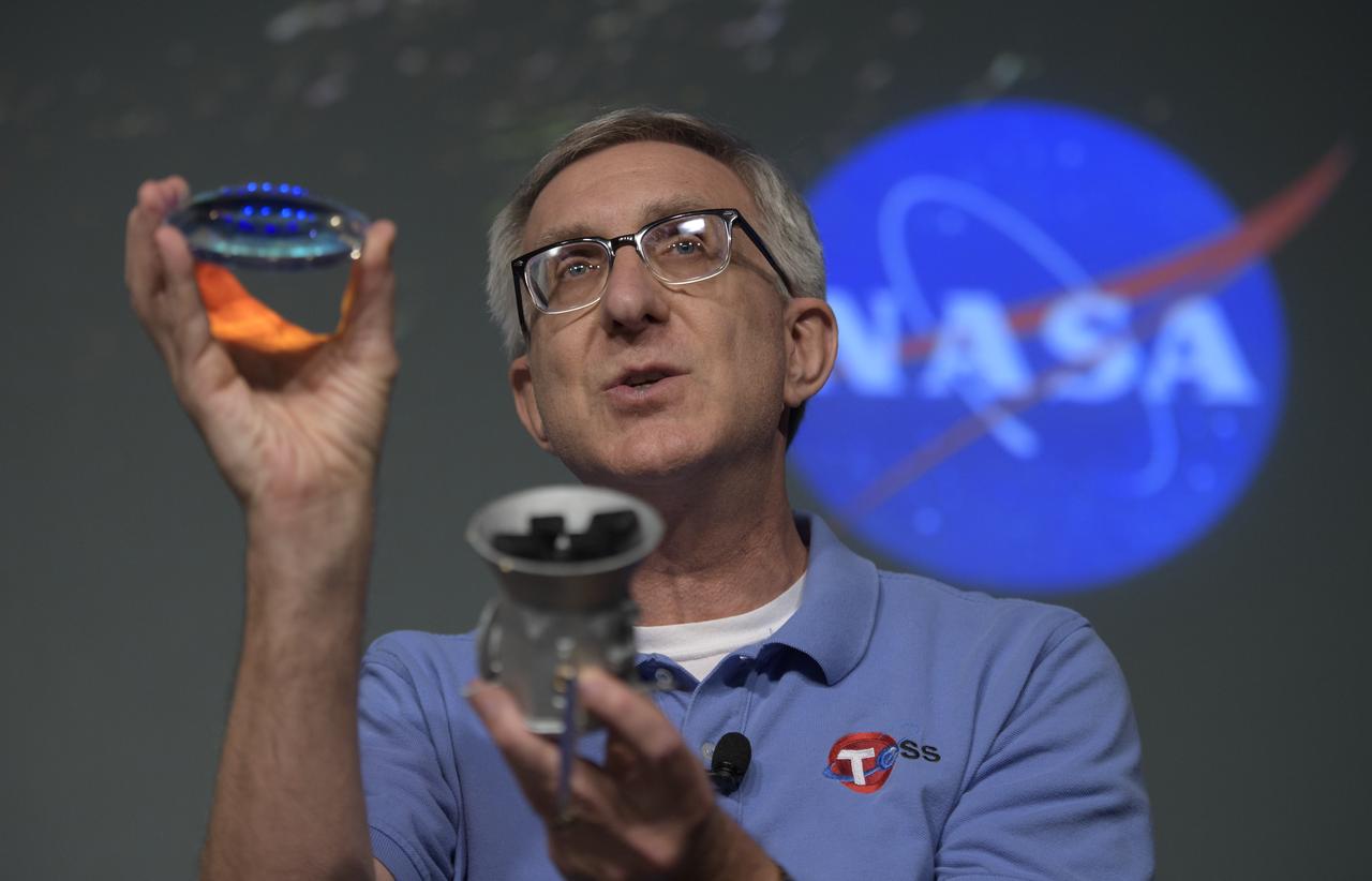 Jeff Volosin, TESS project manager, NASA’s Goddard Space Flight Center, holds a spare camera lens and a model of the Transiting Exoplanet Survey Satellite (TESS) during a media briefing, Wednesday, March 28, 2018 at NASA Headquarters in Washington. Photo Credit: (NASA/Bill Ingalls)