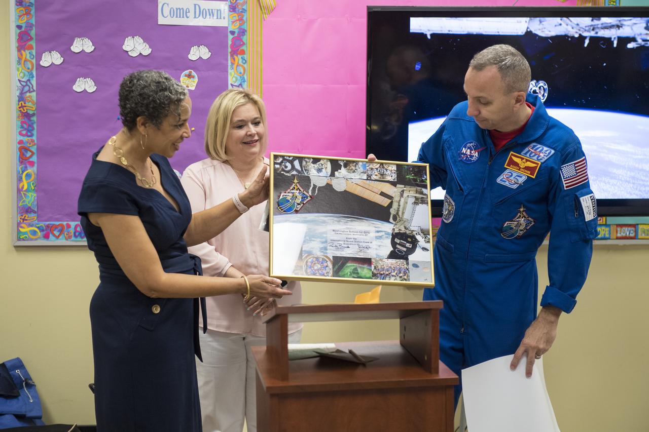 NASA astronaut Randy Bresnik, right, and his friend Shiela, center, present the principle of the school Dr. Beth Reaves, with a montage of images and items from Expedition 53, Friday, May 11, 2018 at the Washington School for Girls in Washington. Photo Credit: (NASA/Aubrey Gemignani)